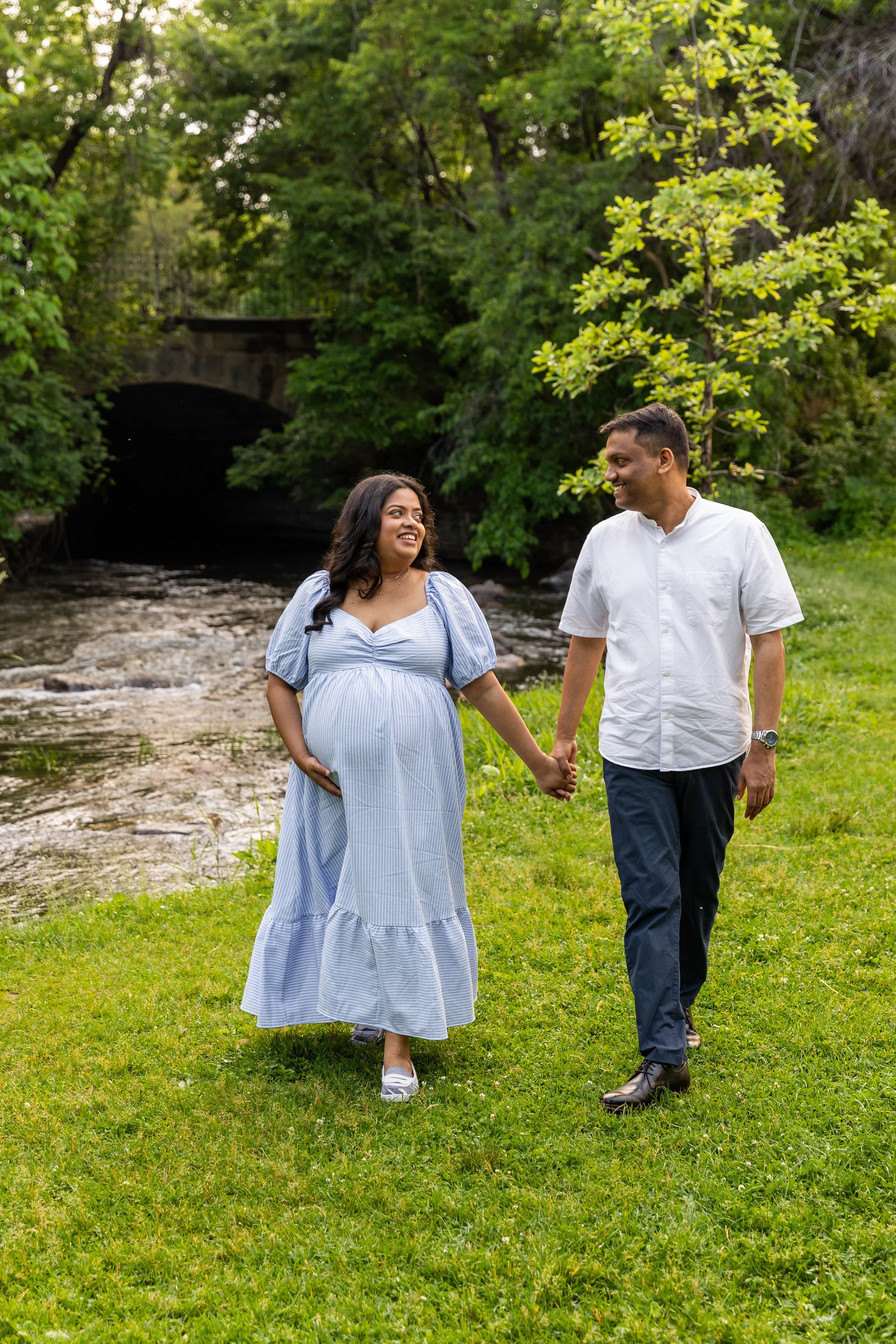 Maternity session - A mother and father walk hand in hand while smiling at each other at Minnehaha Falls Park 