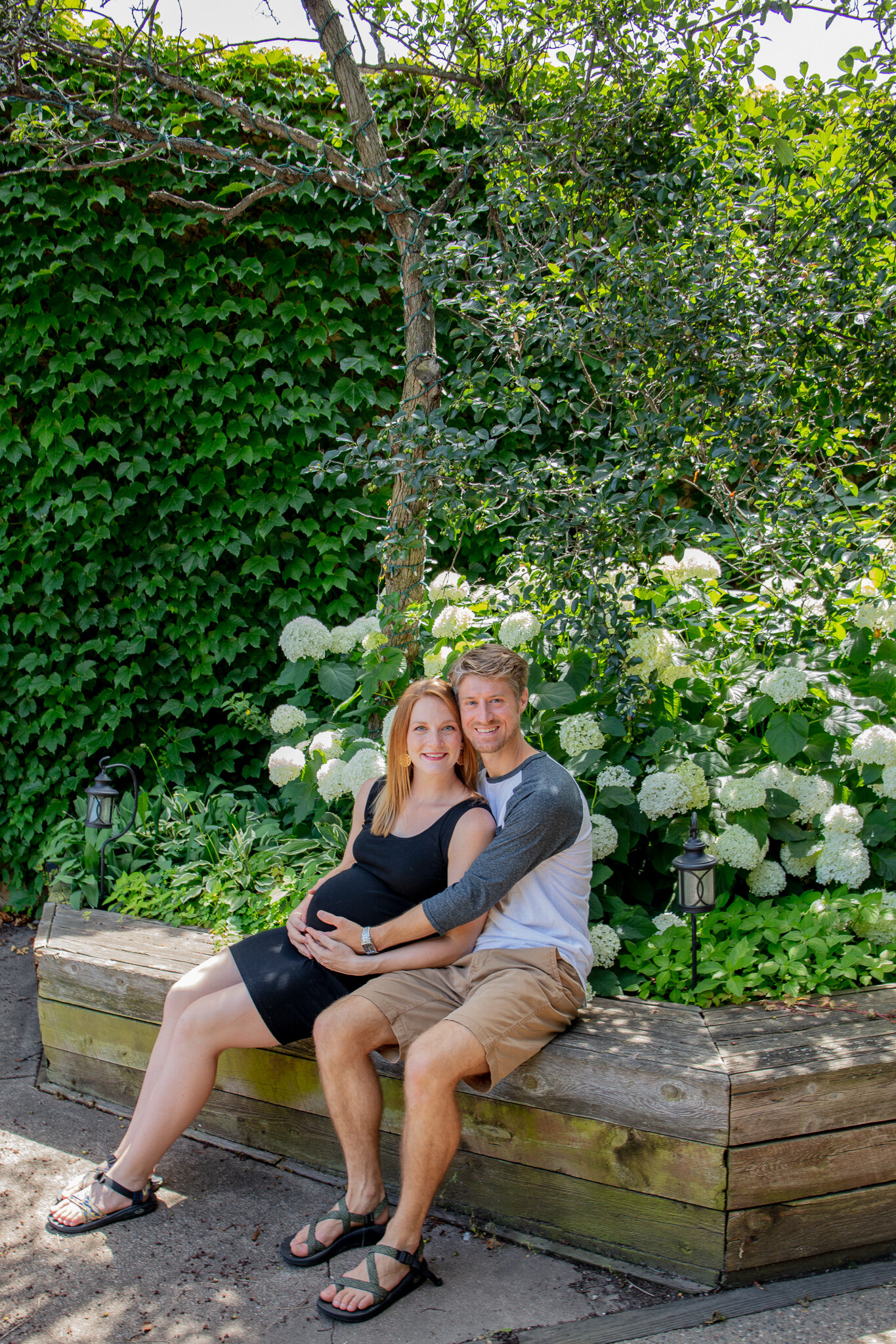 Maternity session, father and mother sitting in a garden holding baby bump