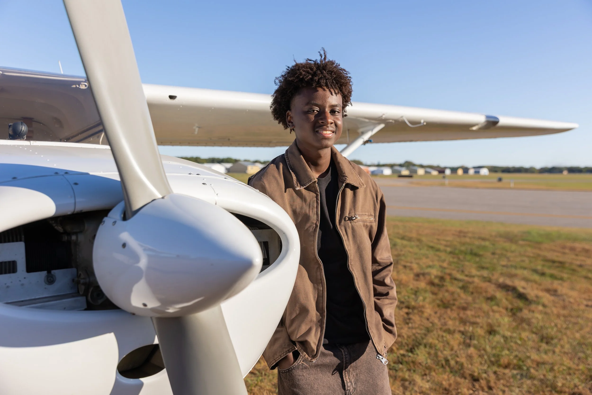 A Maple Grove high school senior stands against a Cessna airplane near the propeller in the Crystal airport smiling at the camera for their senior photos.