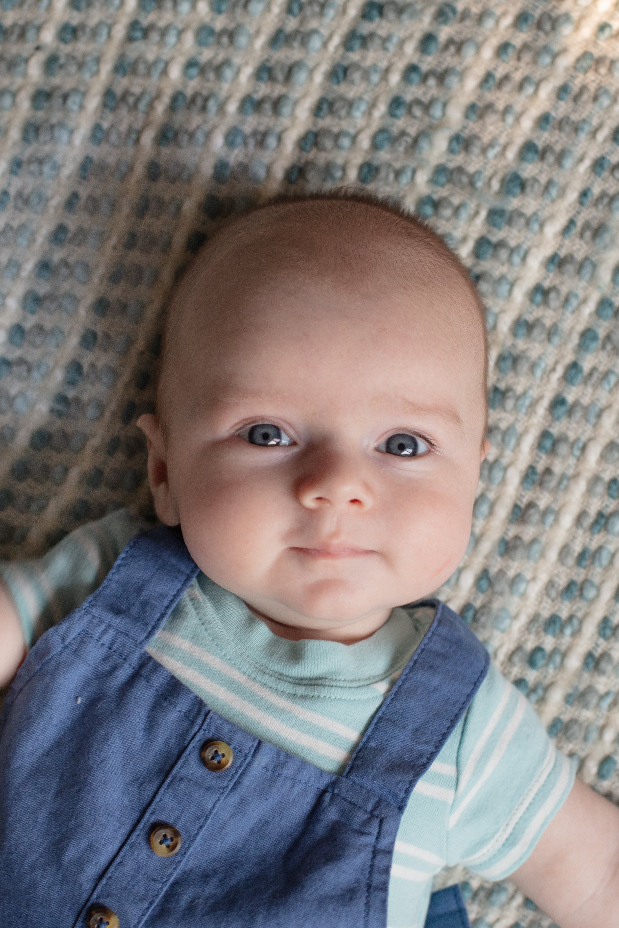 Close up of baby laying down on his back while looking up at the camera.