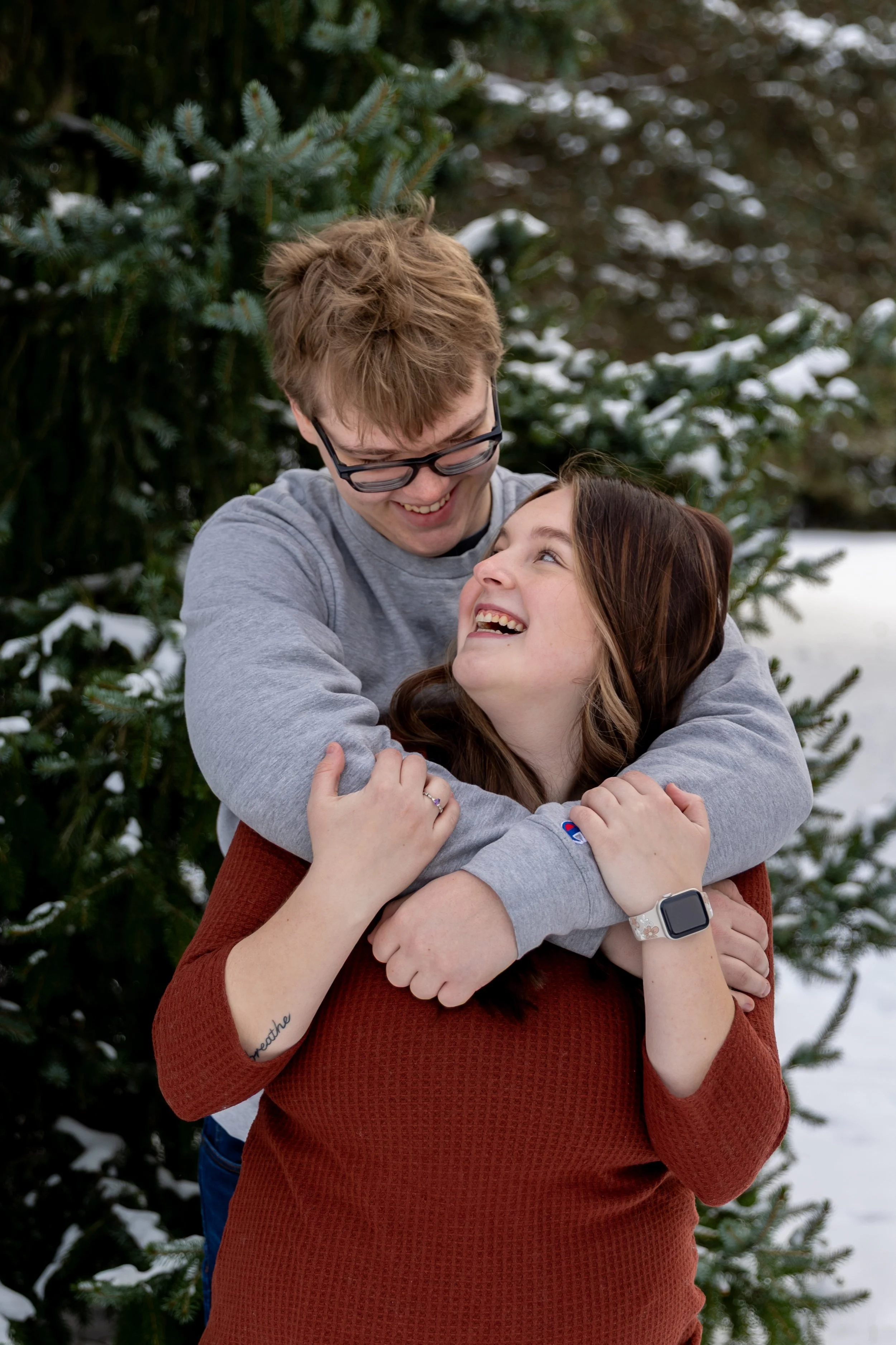 Minneapolis couples photography - A couple embrace and smile at each other with the man looping his arms around her from behind in a winter scene at Arneson Acres Park in Edina, MN.