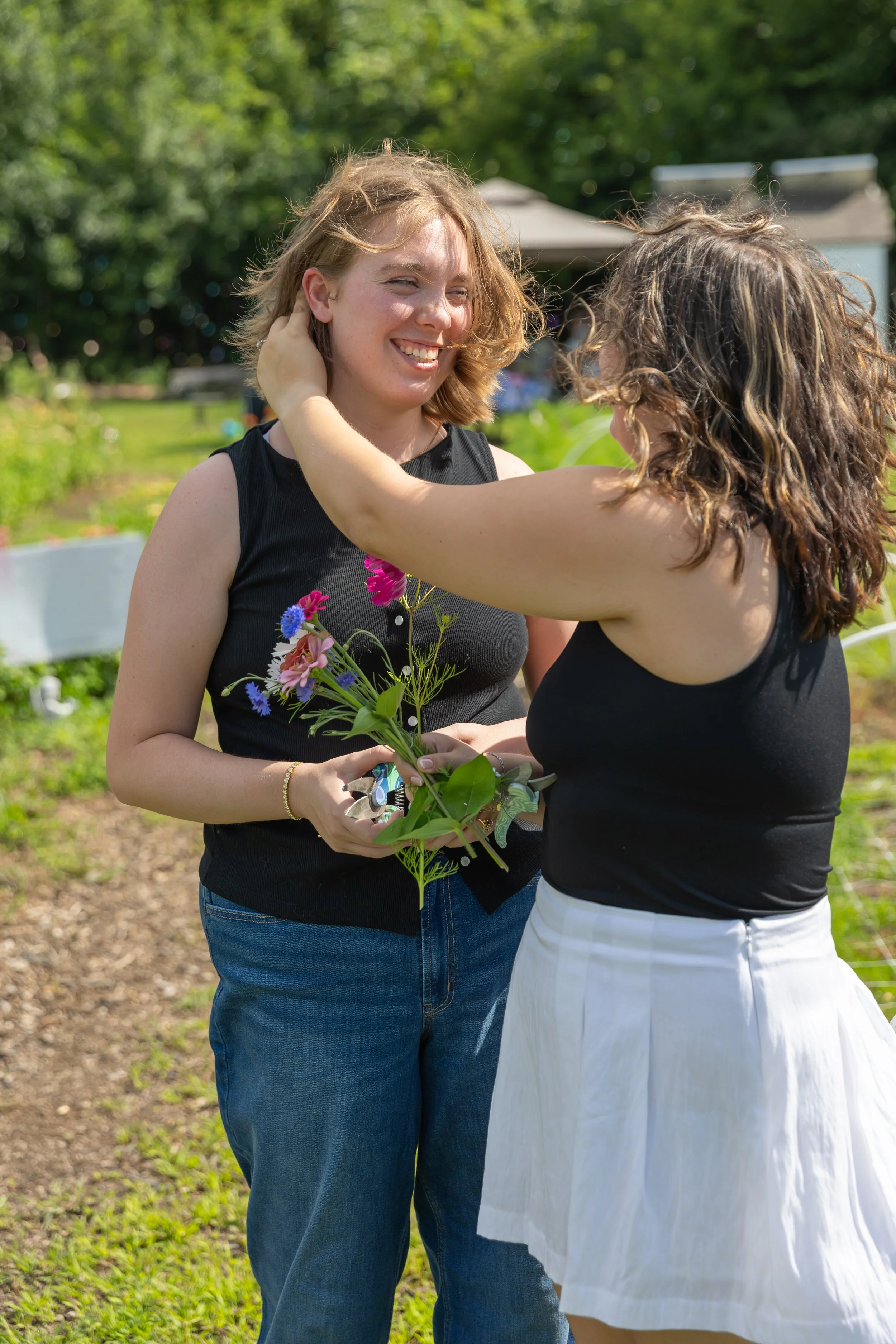Minneapolis couples photography - A couple pick flowers together and brushes the hair out of their faces at Lakeside Farm and Flowers in Cologne, MN.