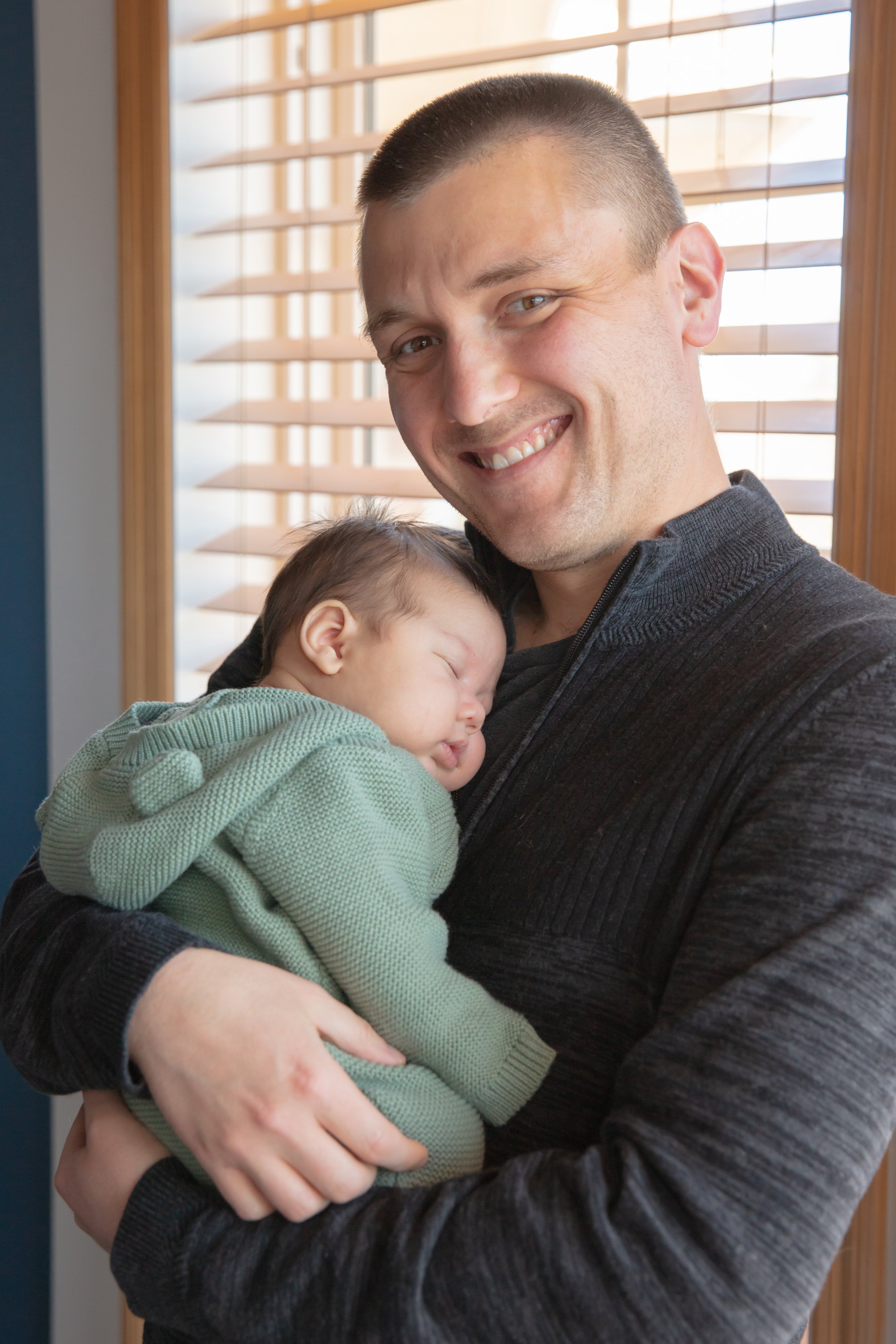 Dad holds his baby in his arms as he smiles at the camera.