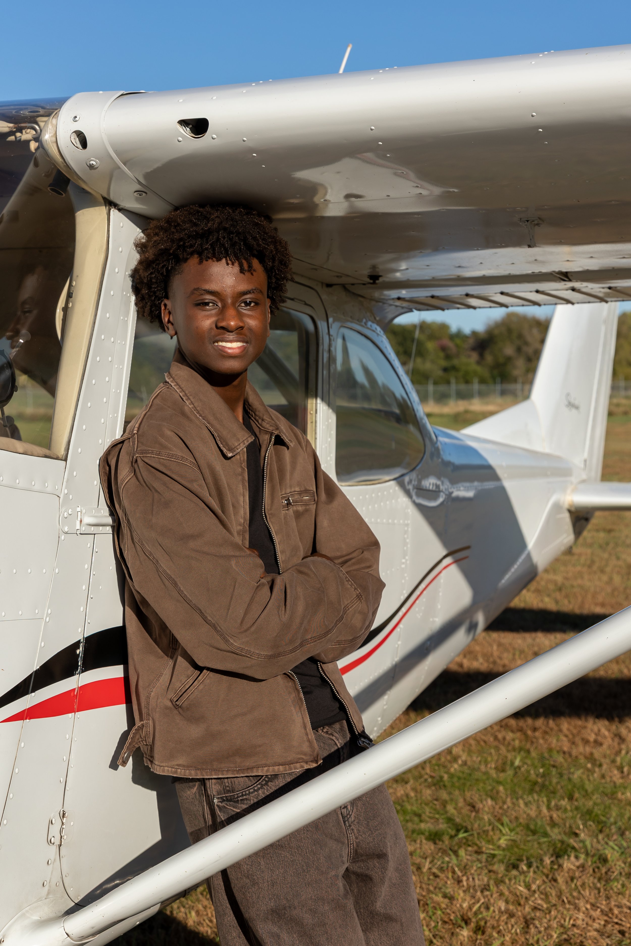 A Maple Grove high school senior leans against a Cessna airplane in the Crystal airport smiling at the camera for their senior photos.
