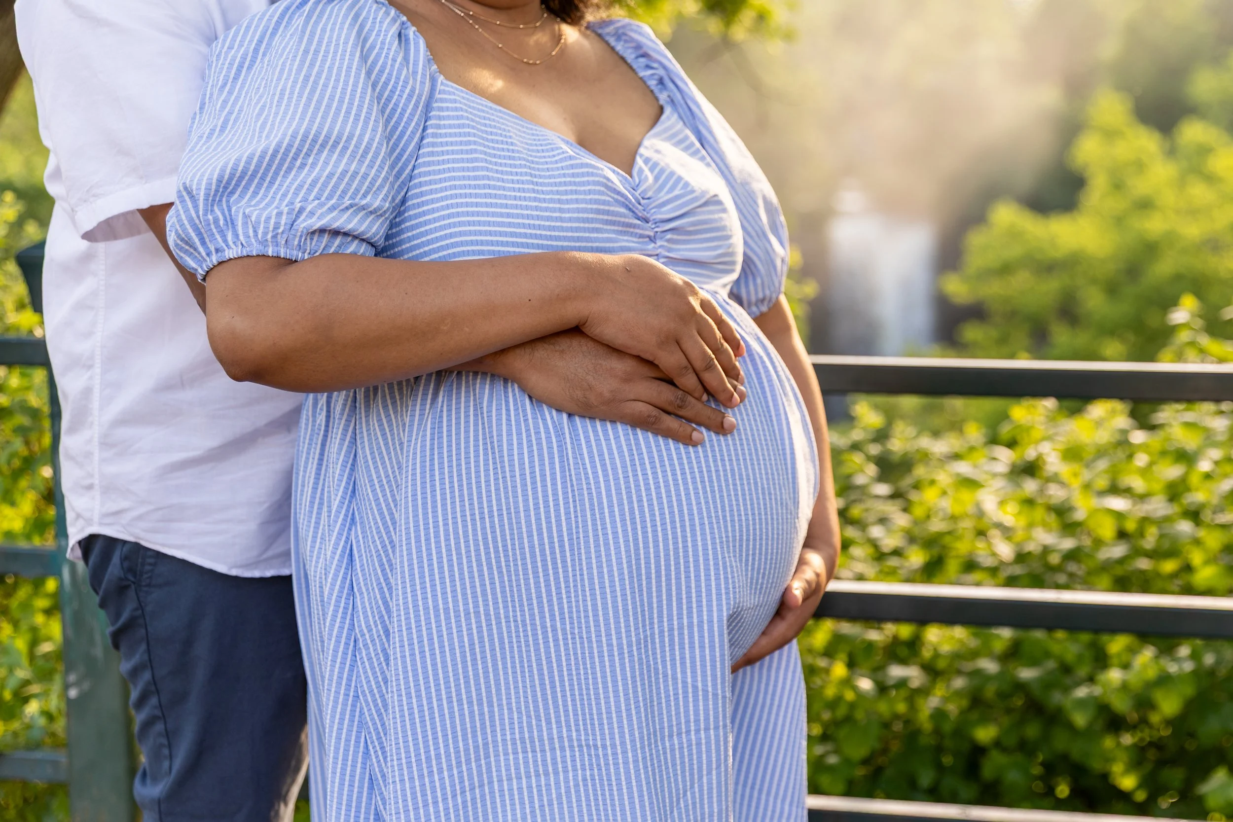 Maternity session - close up of father and mother standing together cradling the baby bump while at Minnehaha Falls Park with the waterfall in the background