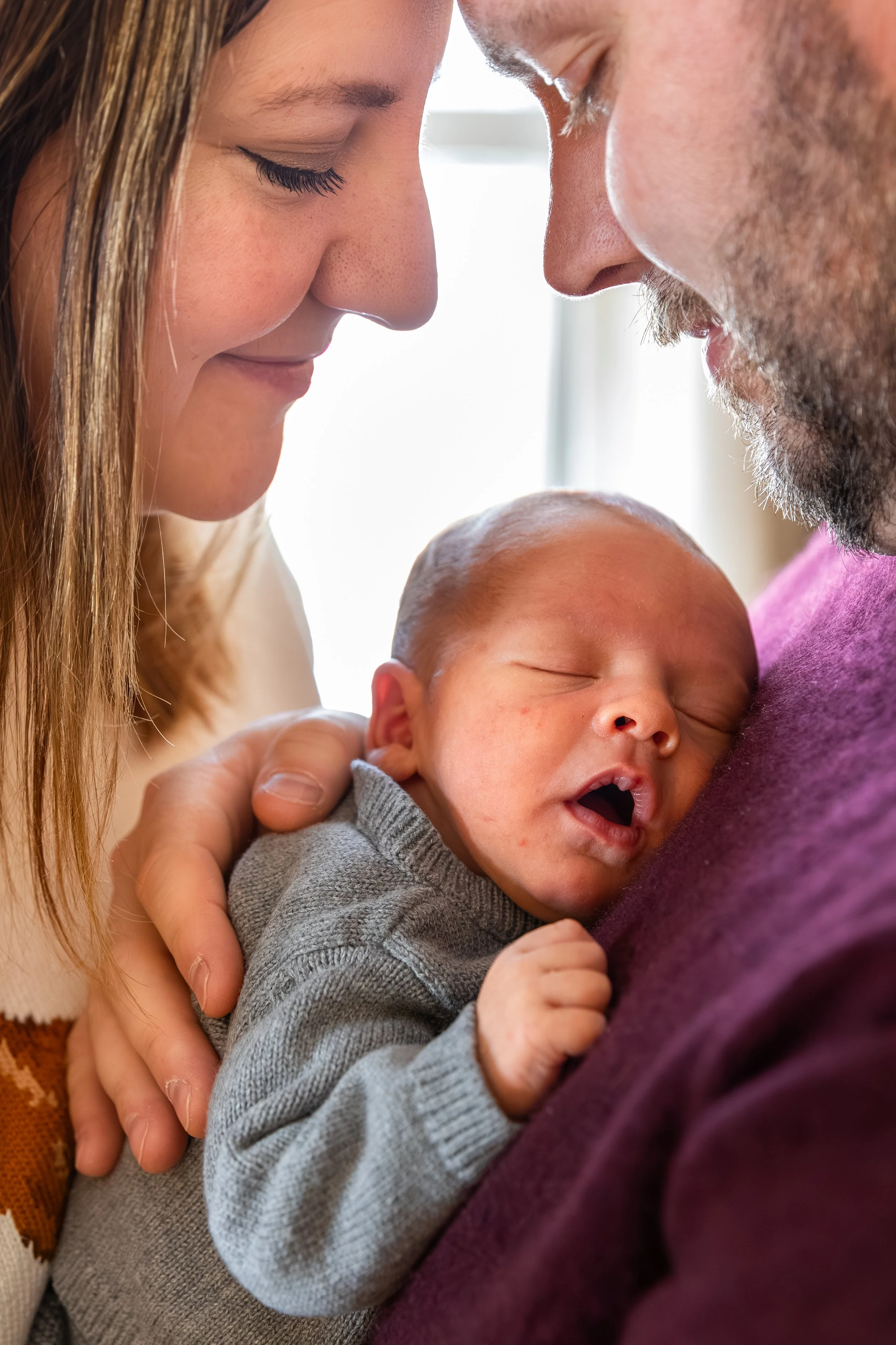 Minneapolis in-home newborn photography session - Up close image of baby being held on dads chest with mom and dad surrounding the baby looking down at the newborn.