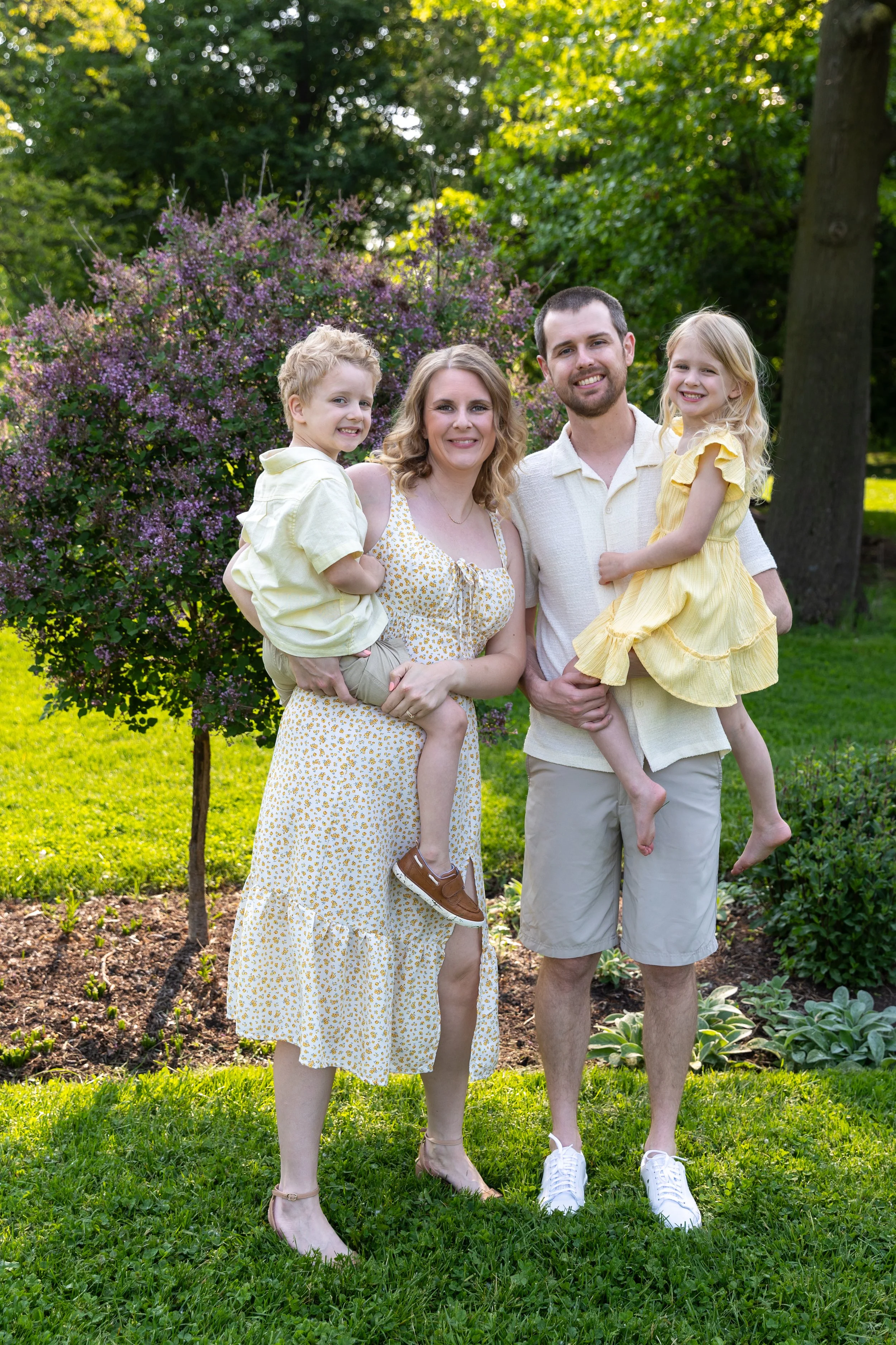 Minneapolis Family Photography May Mini Session- A mother and father together holding their twin son and daughter as they all smile at the camera together. They are at Lyndale Rose Garden in Minneapolis, MN. 