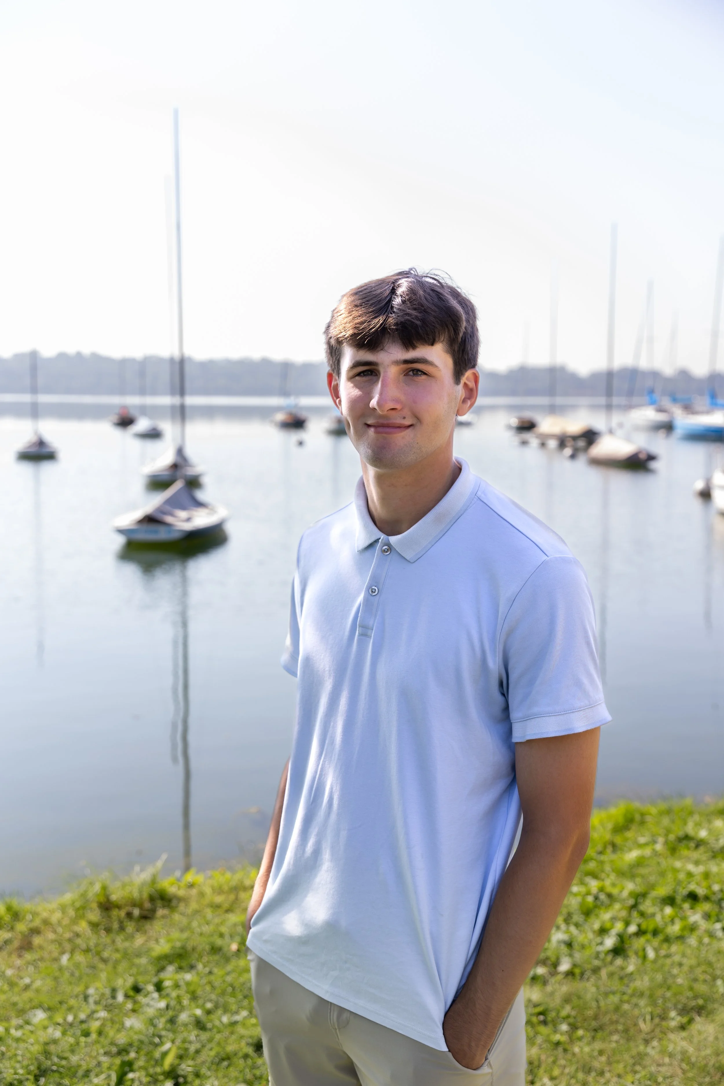 A Minneapolis high school stands smiling at the camera in front of sailboats at Lake Harriet posing for their senior photos.