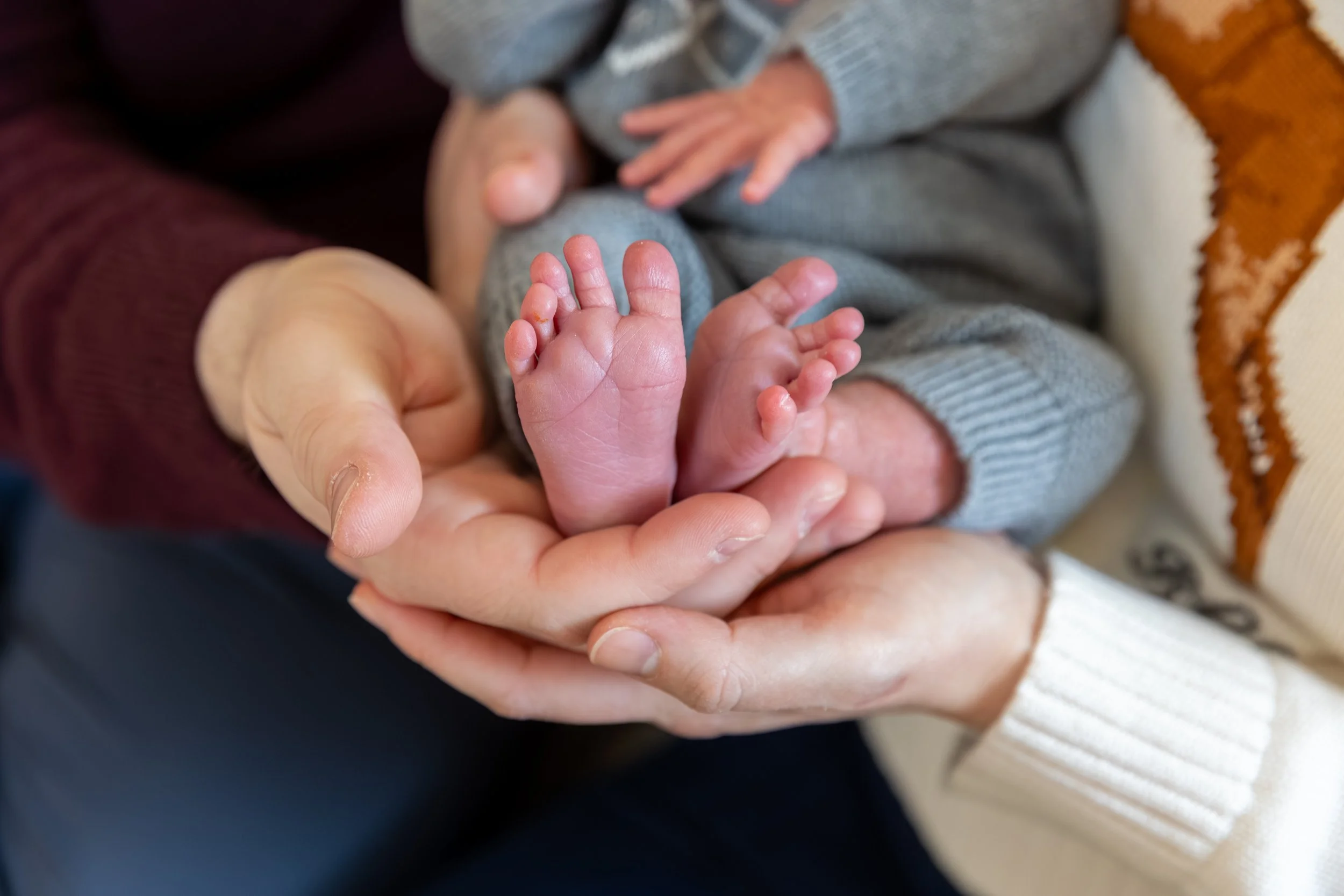 Minneapolis in-home newborn photography session - Up close image of baby being held in mom and dads arms with the image focused on the newborns feet being cradled in the parents hands.