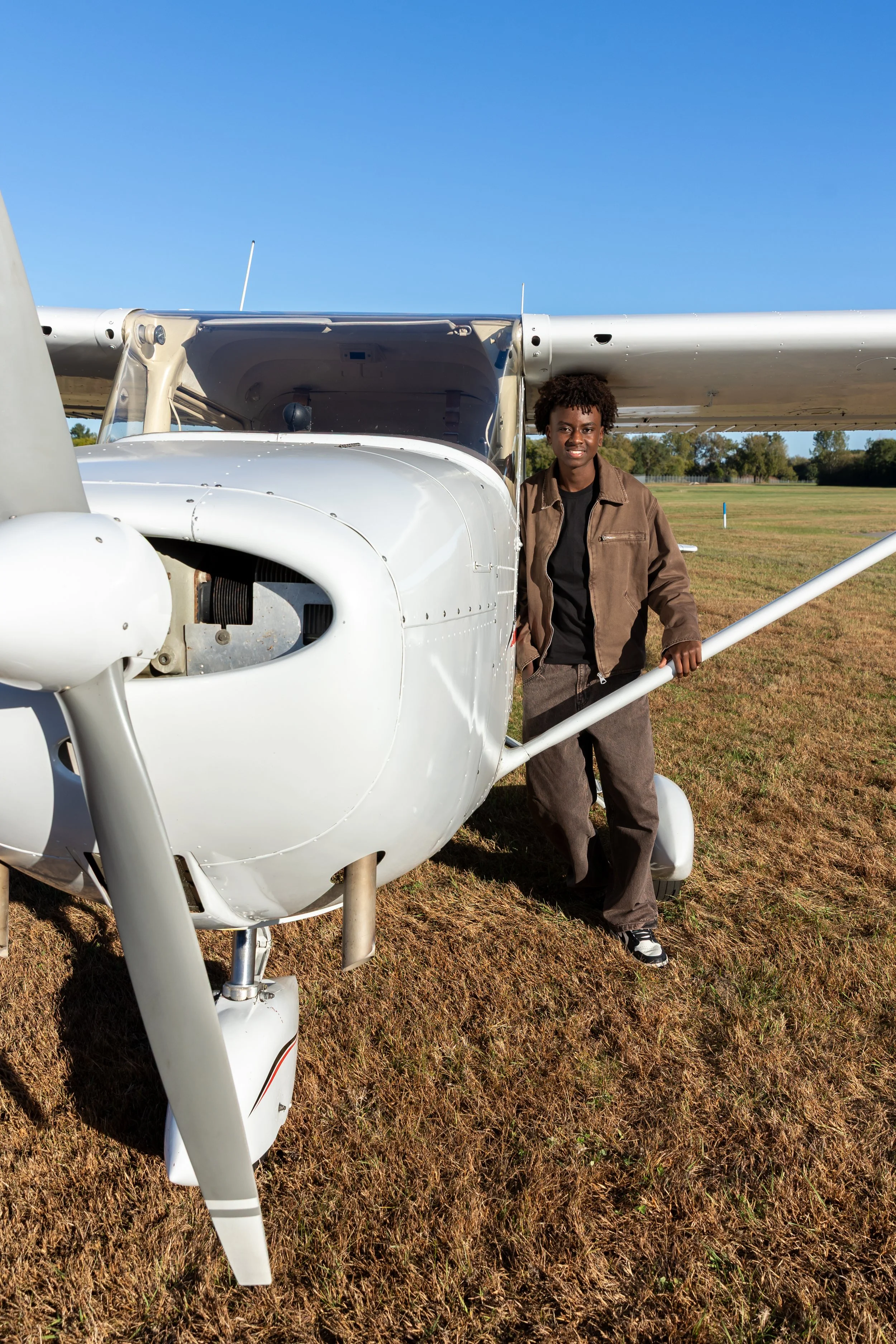 A Maple Grove high school senior stands against a Cessna airplane in the Crystal airport smiling at the camera for their senior photos.