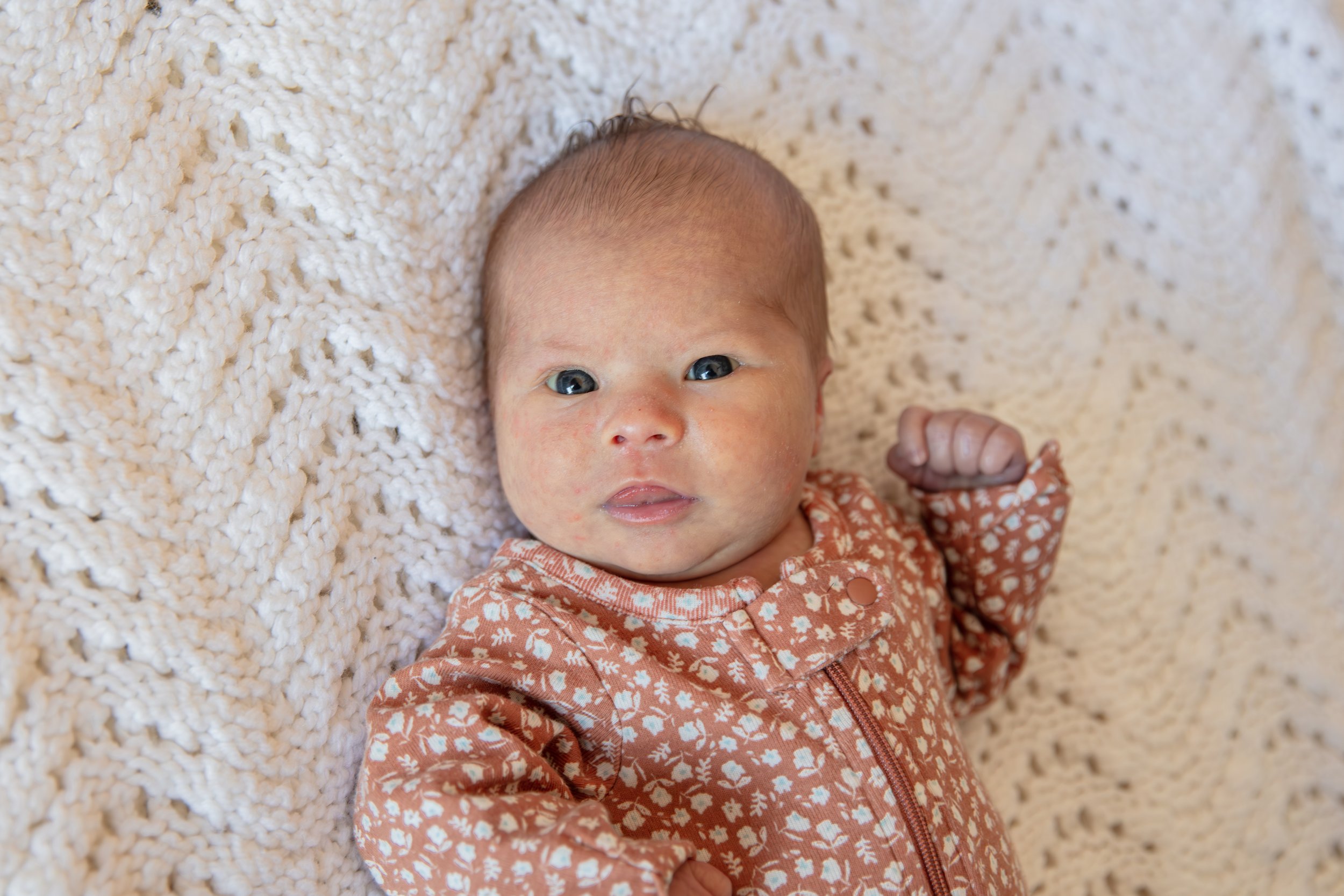 Close up of baby looking at the camera while laying on a blanket.