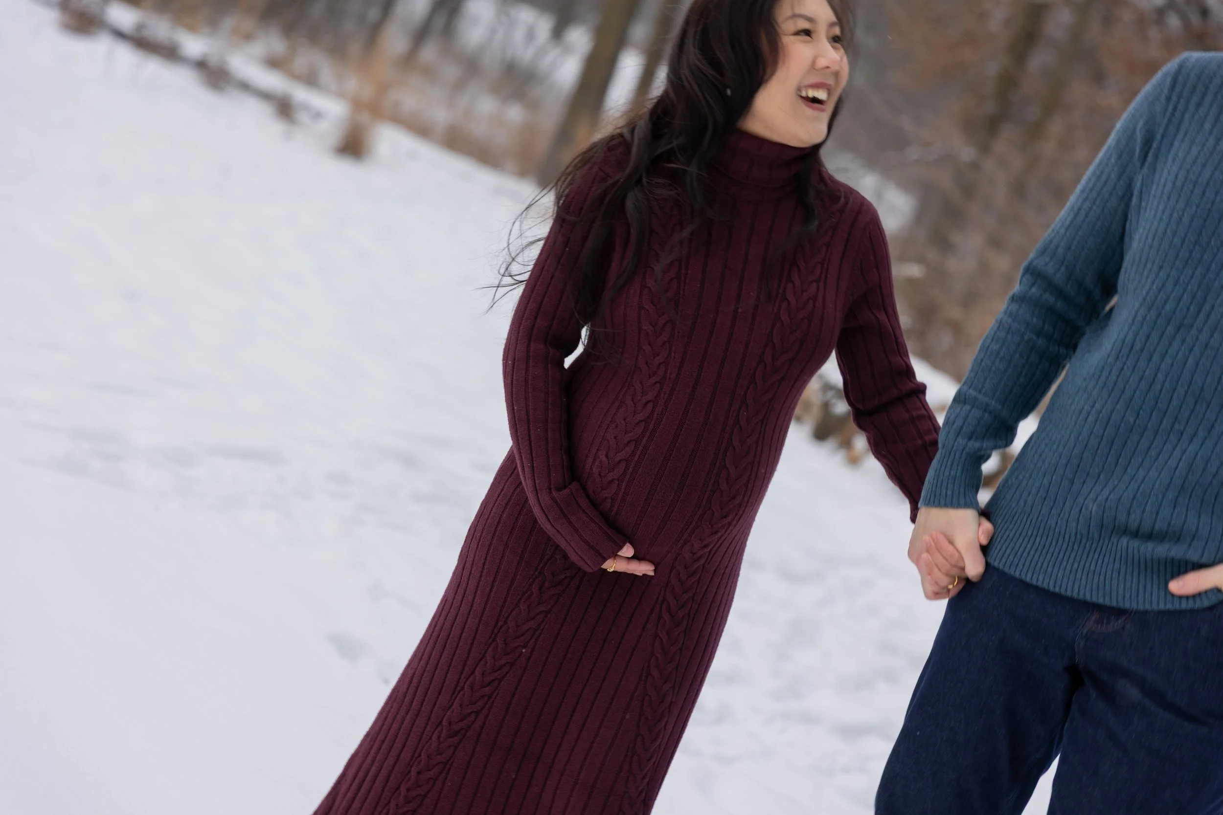 Maternity session - close up of father and mother holding hands walking towards the camera with the mother smiling at the father while cradling the baby bump in Minnetonka Mills Park in Hopkins, MN in the winter.