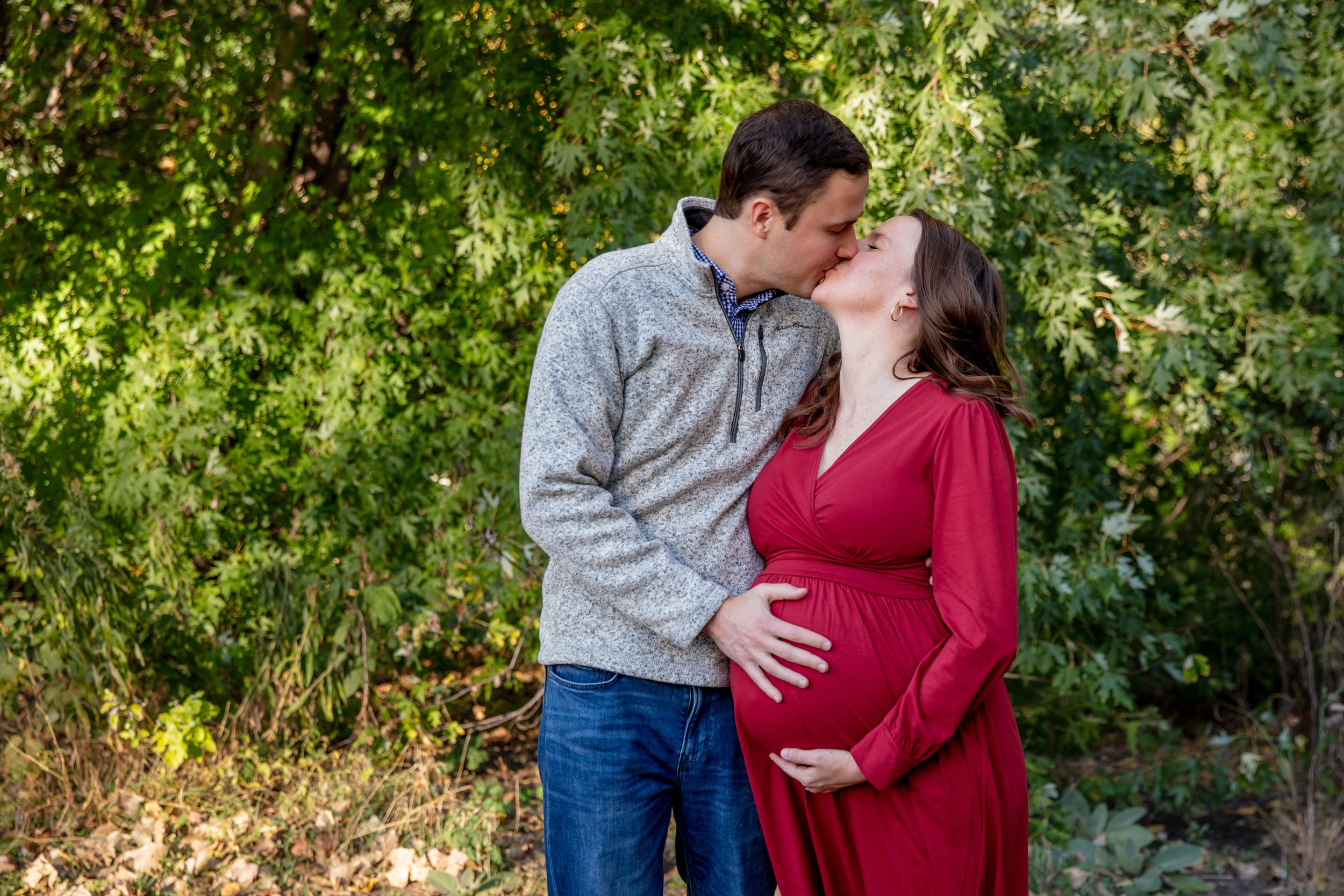 Maternity session, expecting mother and father-to-be kiss each other while each holding the baby bump.