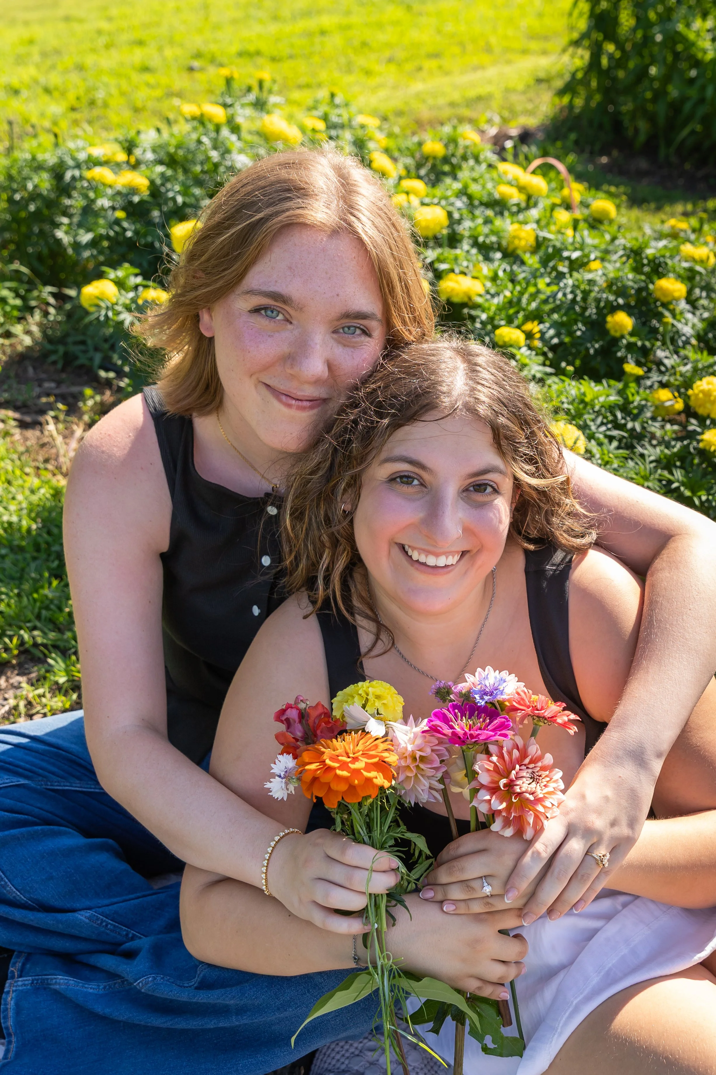 Minneapolis couples photography - A couple sits on a blanket together smiling at the camera holding all the flowers they just picked together at Lakeside Farm and Flowers in Cologne, MN.