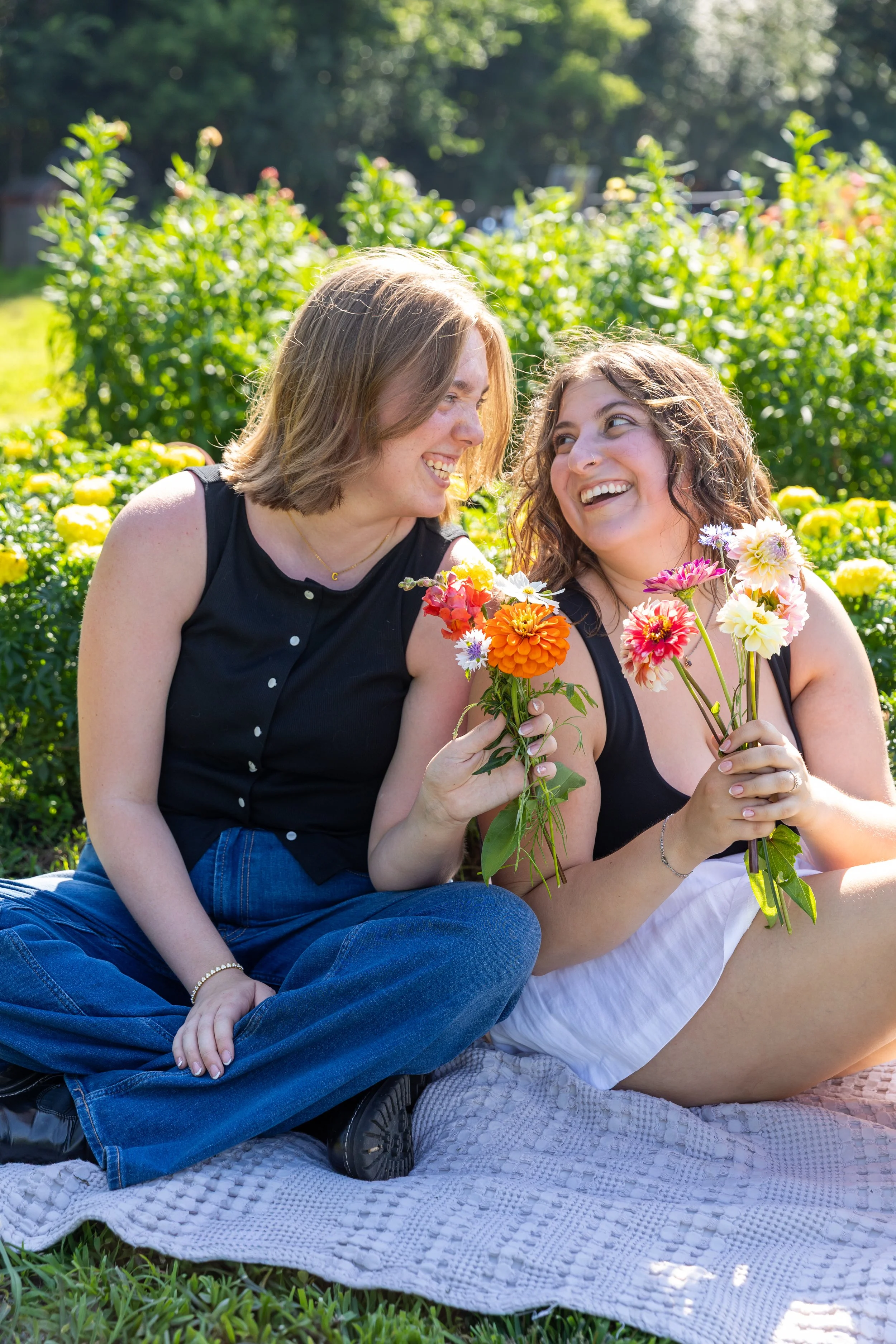 Minneapolis couples photography - A couple sits on a blanket together smiling at each other holding all the flowers they just picked together at Lakeside Farm and Flowers in Cologne, MN.