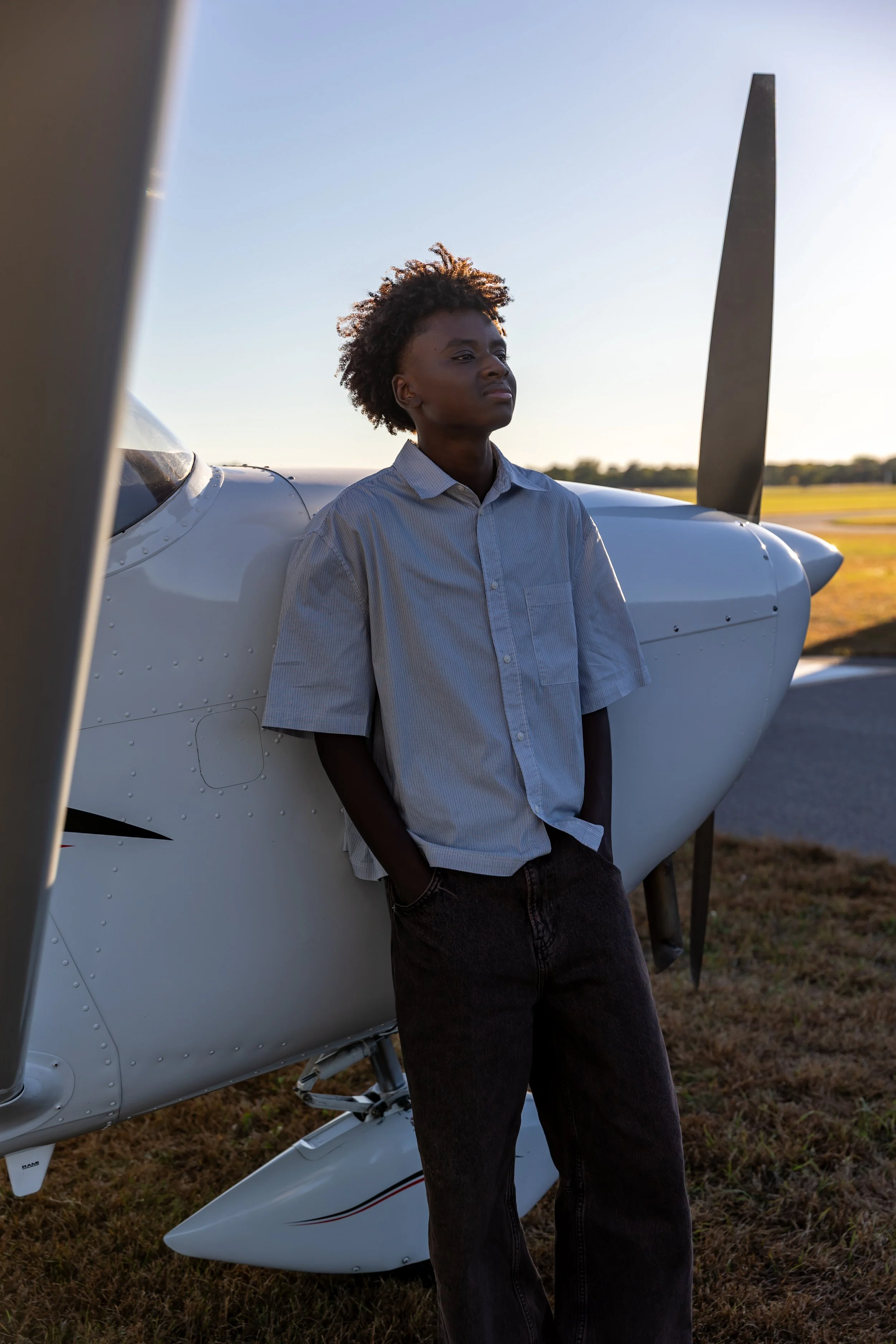 A Maple Grove high school senior stands against a Cessna airplane in the Crystal airport casually looking away for their senior photos.