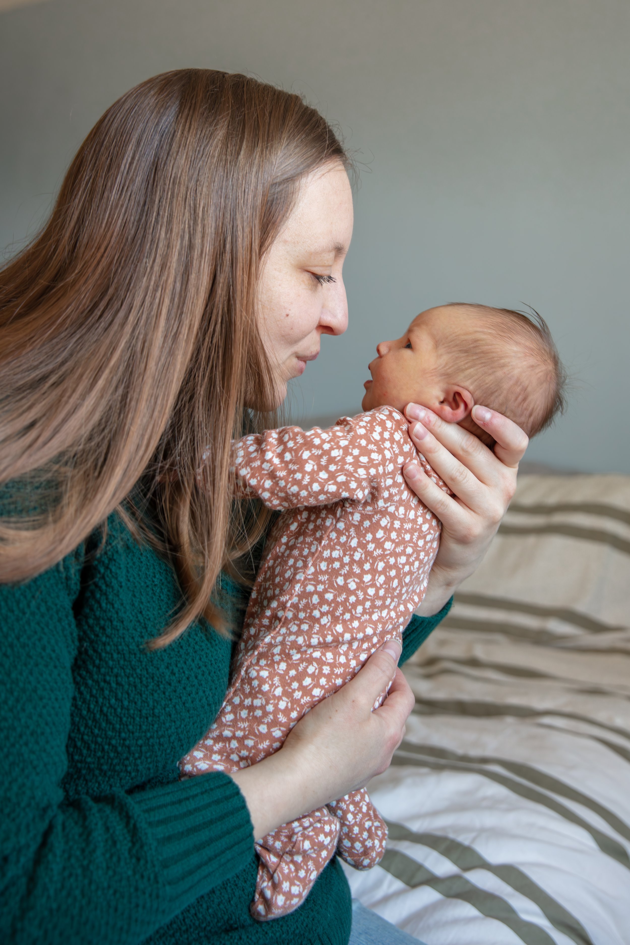 A mother holds her newborn in front of her cooing at the baby while smiling.