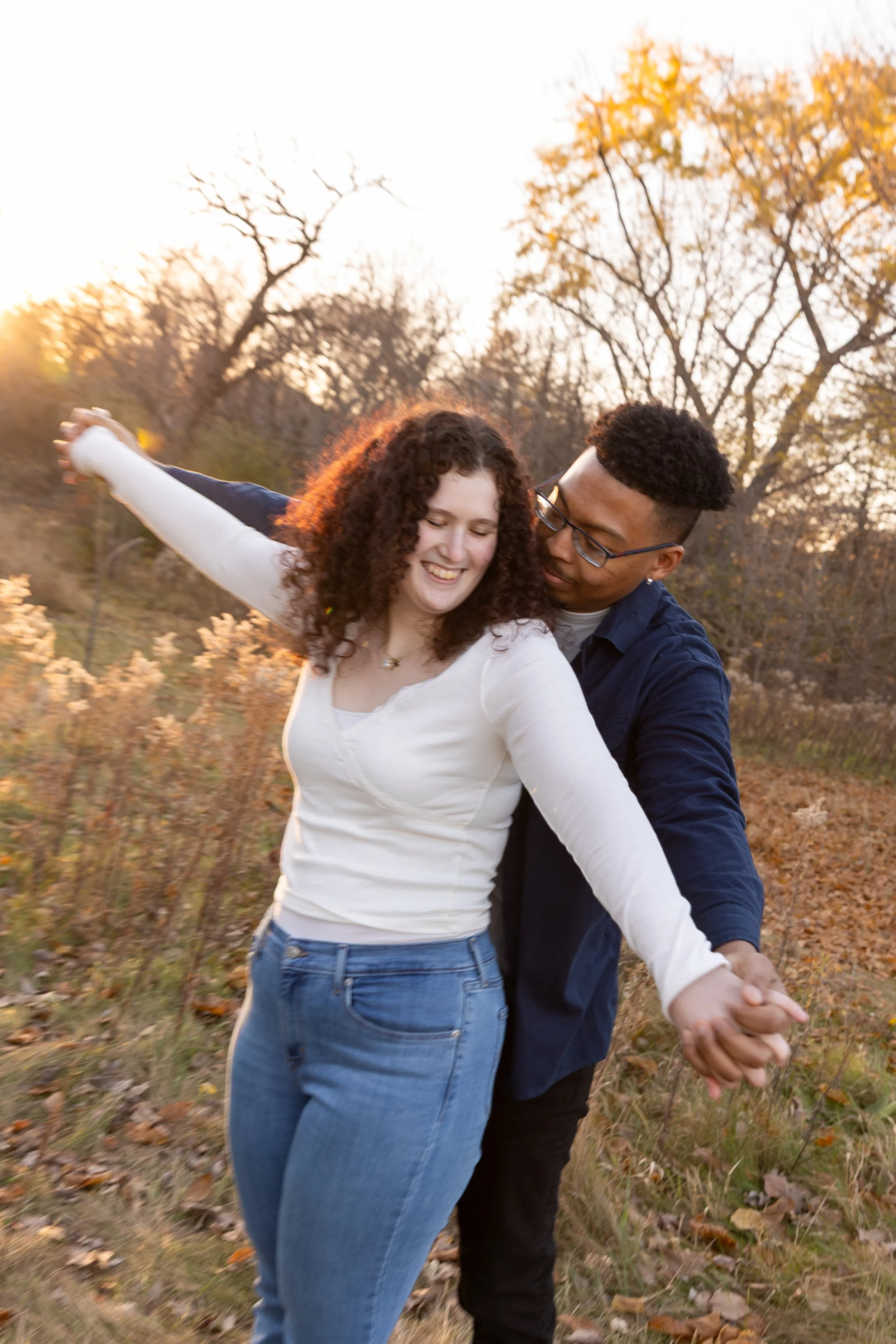 Minneapolis couples photography - A couple hold hands together with their arms extended moving around with the man behind the woman's back and smile while at Minnehaha Falls Park in Minneapolis, MN. 