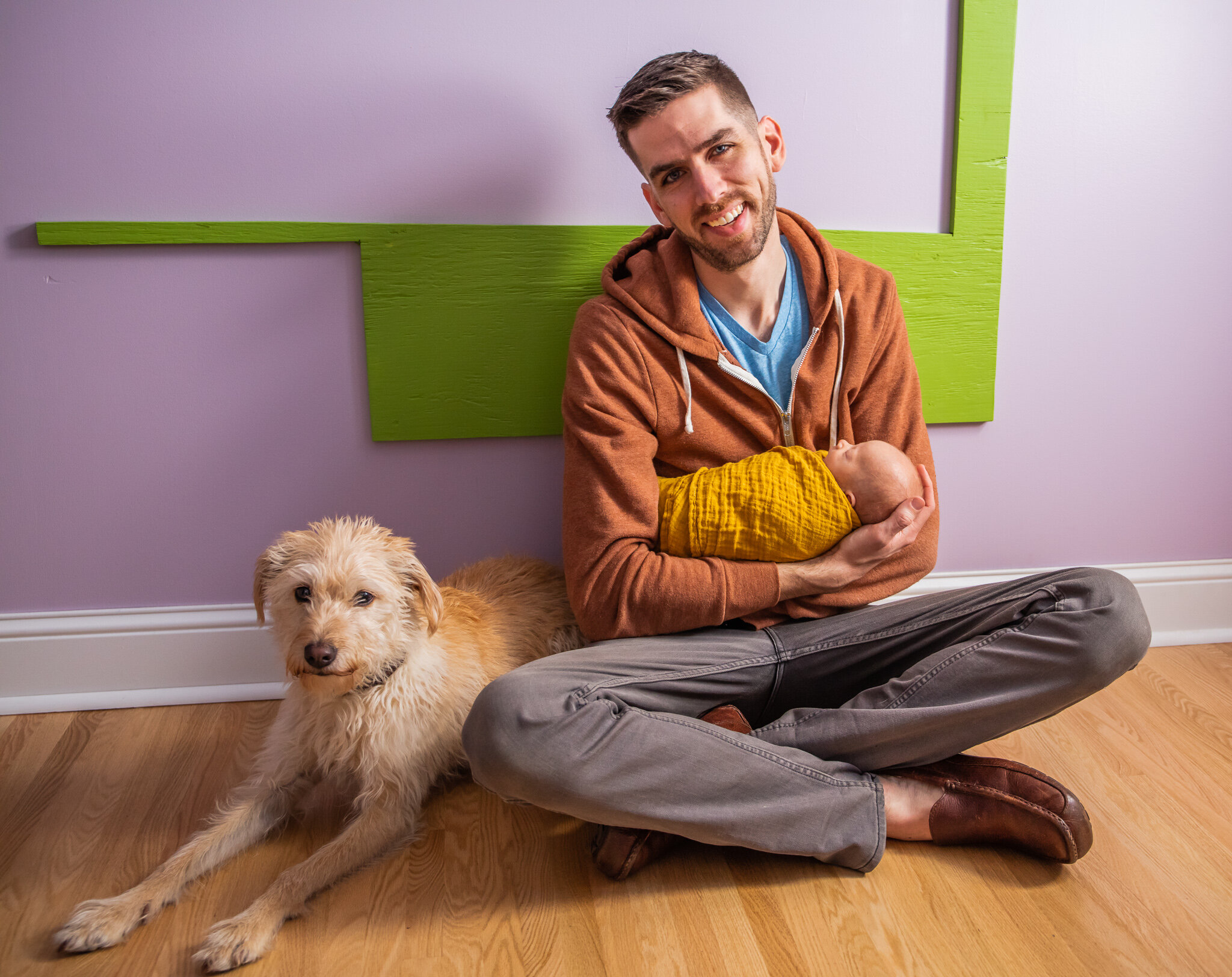 Newborn session, baby asleep in father's arms sitting in home nursery with dog