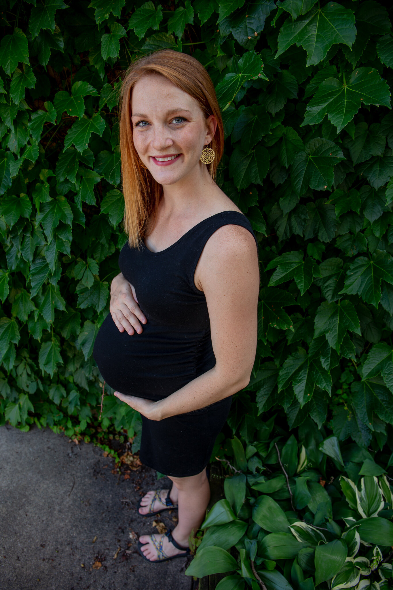 Maternity session, Mother holding baby bump against green leaves background