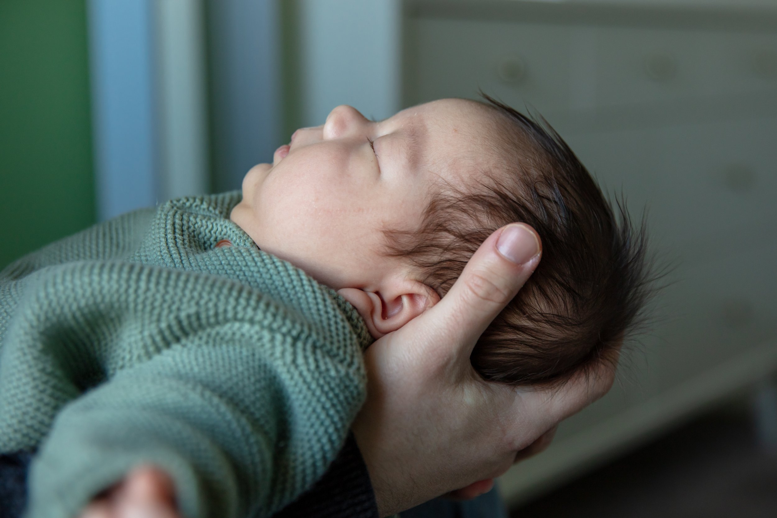 Newborn in-home session, close up of father holding his baby's head in side profile.