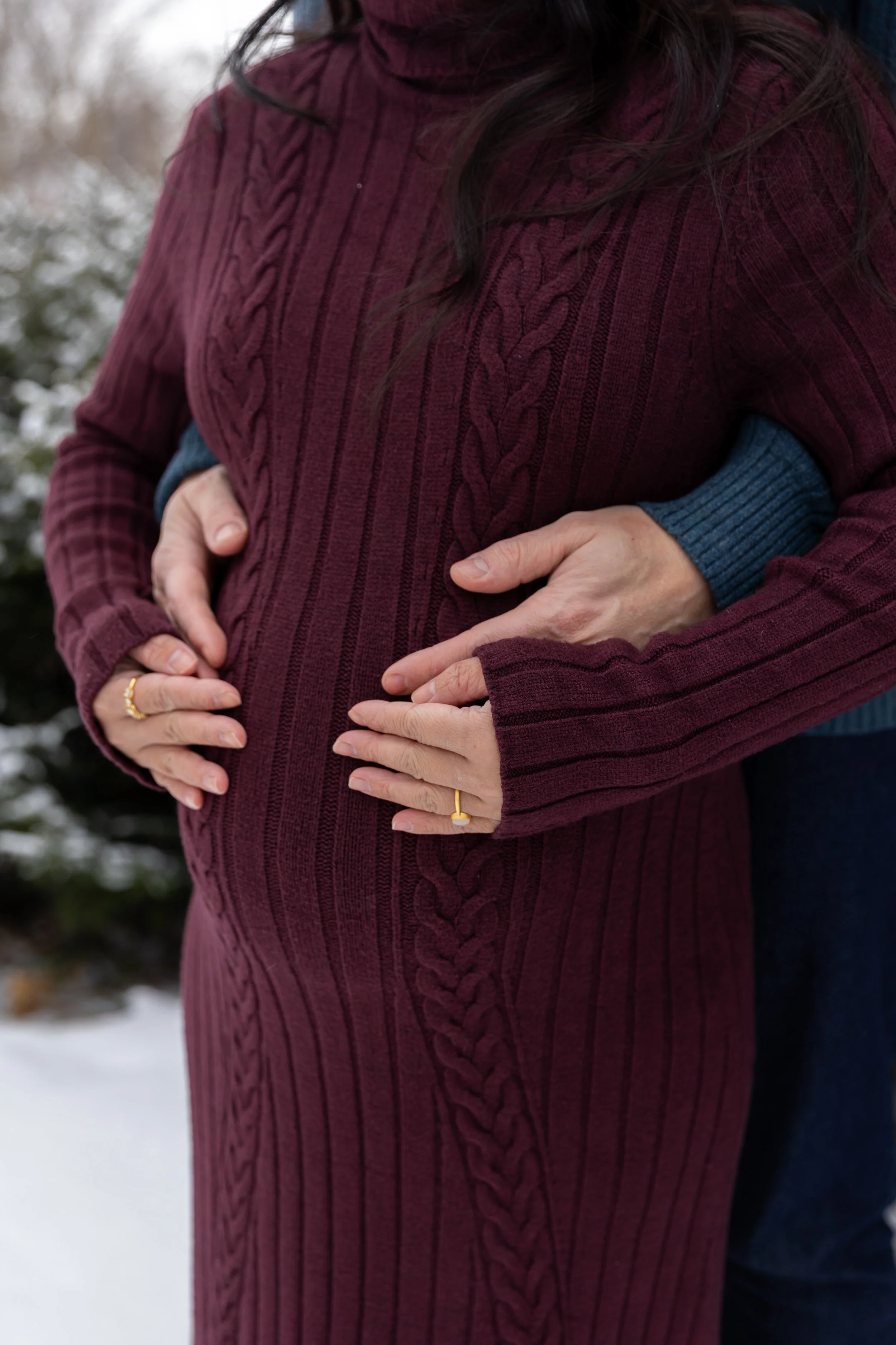 Minneapolis Maternity photography session - A close up of a soon to be mother and father stand embracing each other with their hands wrapped around the bump at Minnetonka Mills Park in Hopkins, MN in the winter.