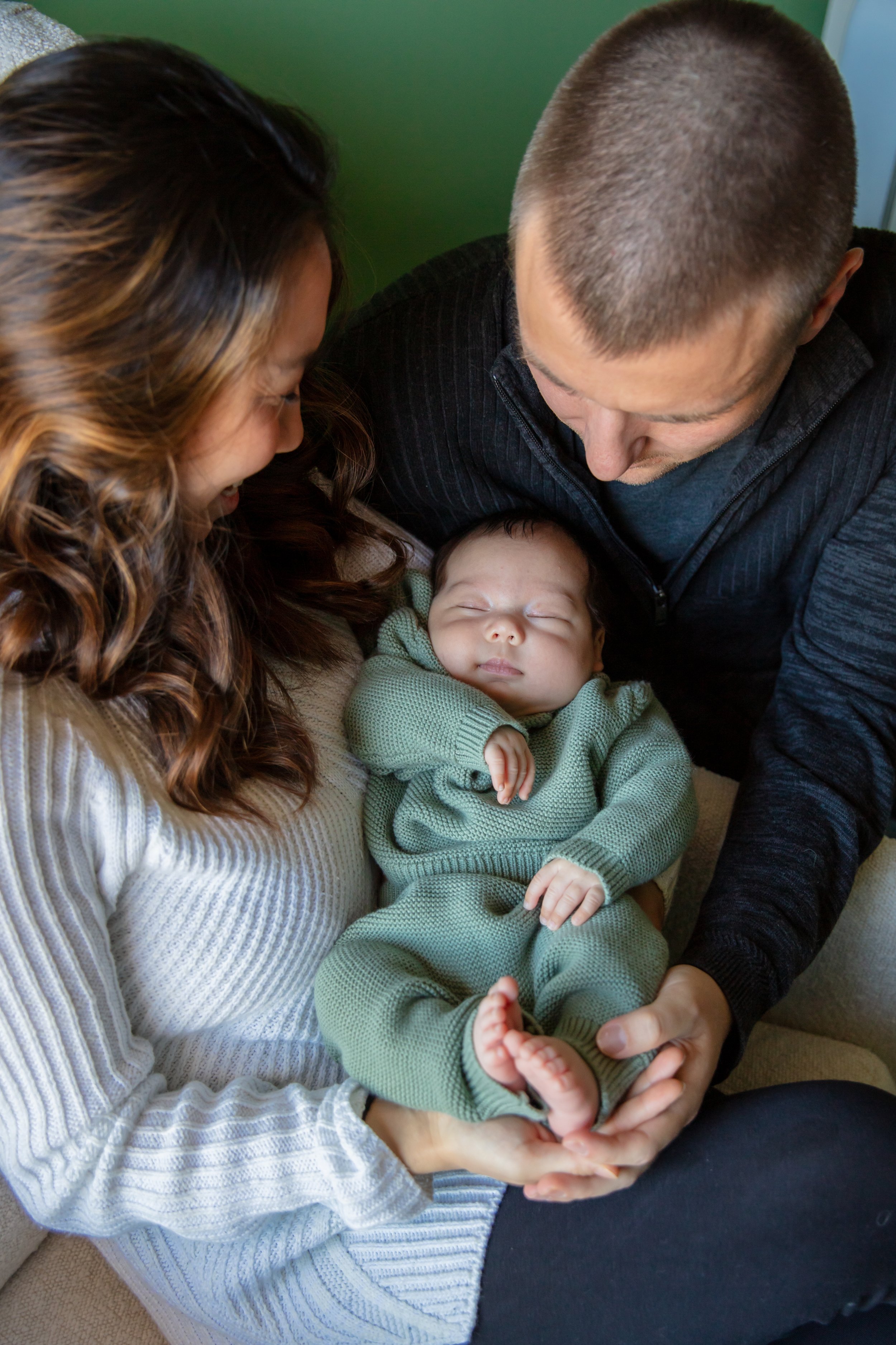 Newborn session, close up of mother and father sitting while holding their baby in their nursery at home.