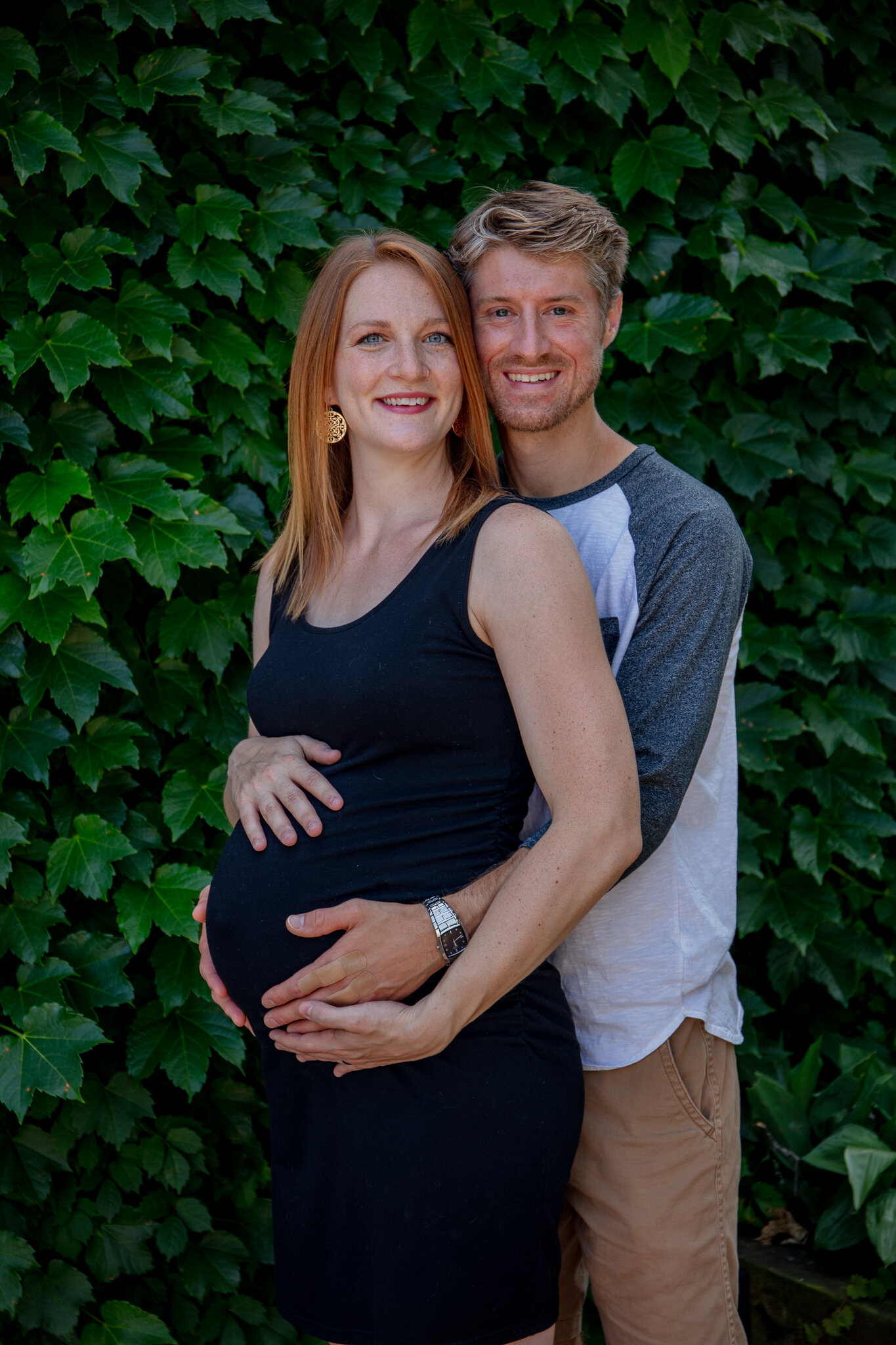Maternity session, Mother and father holding baby bump against green leaves background