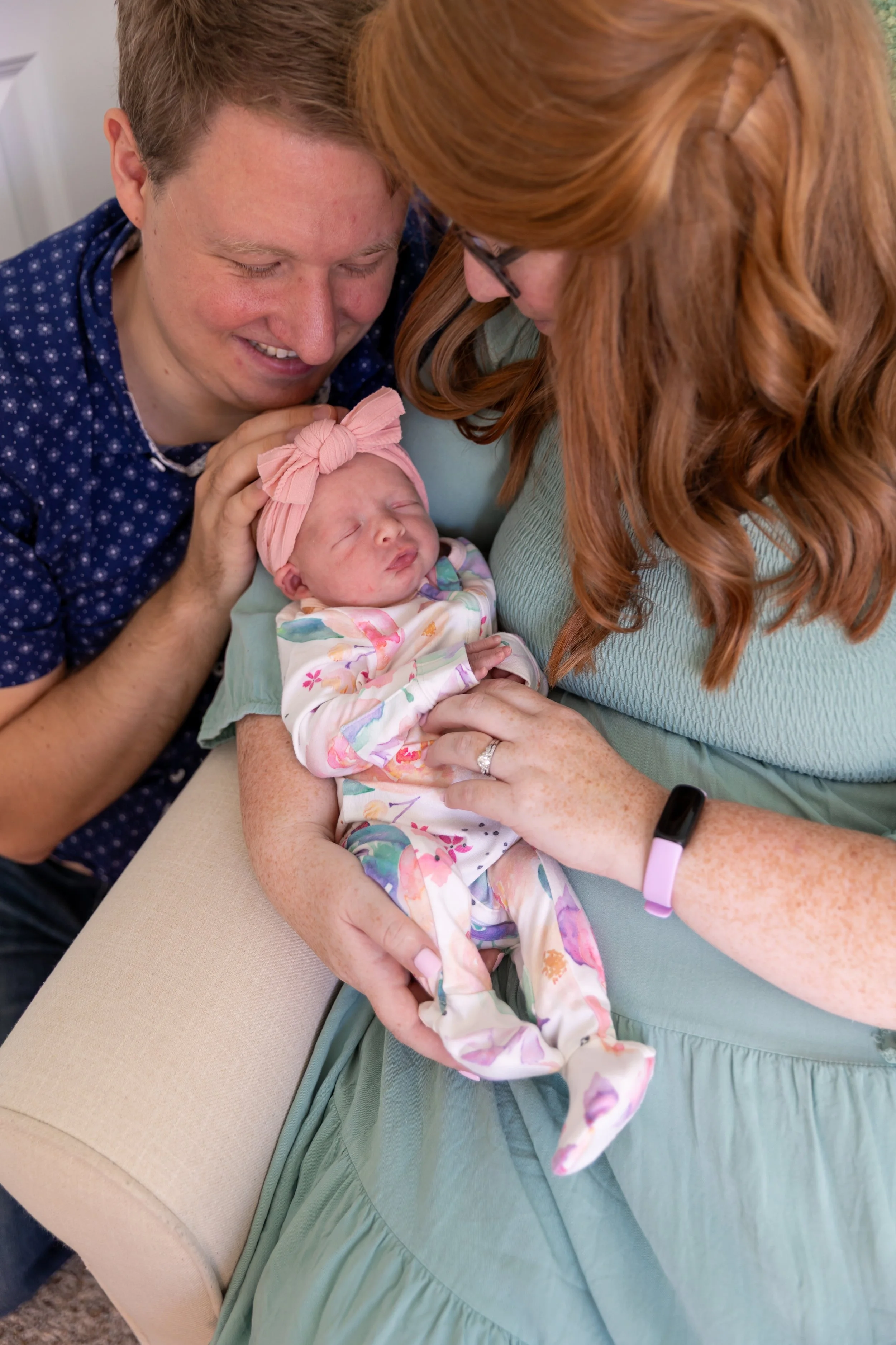Minneapolis in-home newborn photography session - Up close image of baby being held in moms arms with mom and dad surrounding the baby looking down at the newborn.