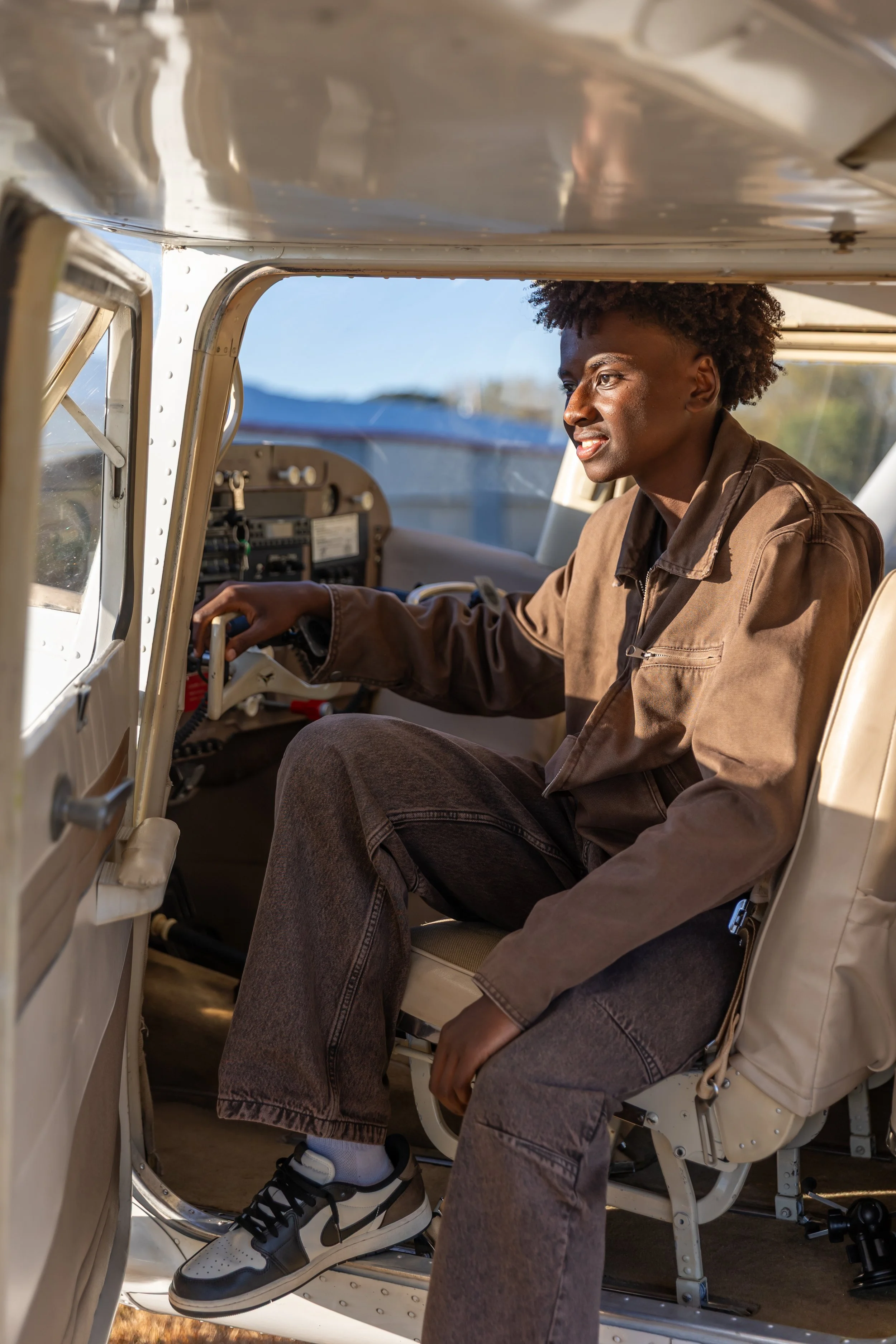 A Maple Grove high school leans out of the door of the cockpit of a Cessna airplane in the Crystal airport smiling for their senior photos while wearing a headset.