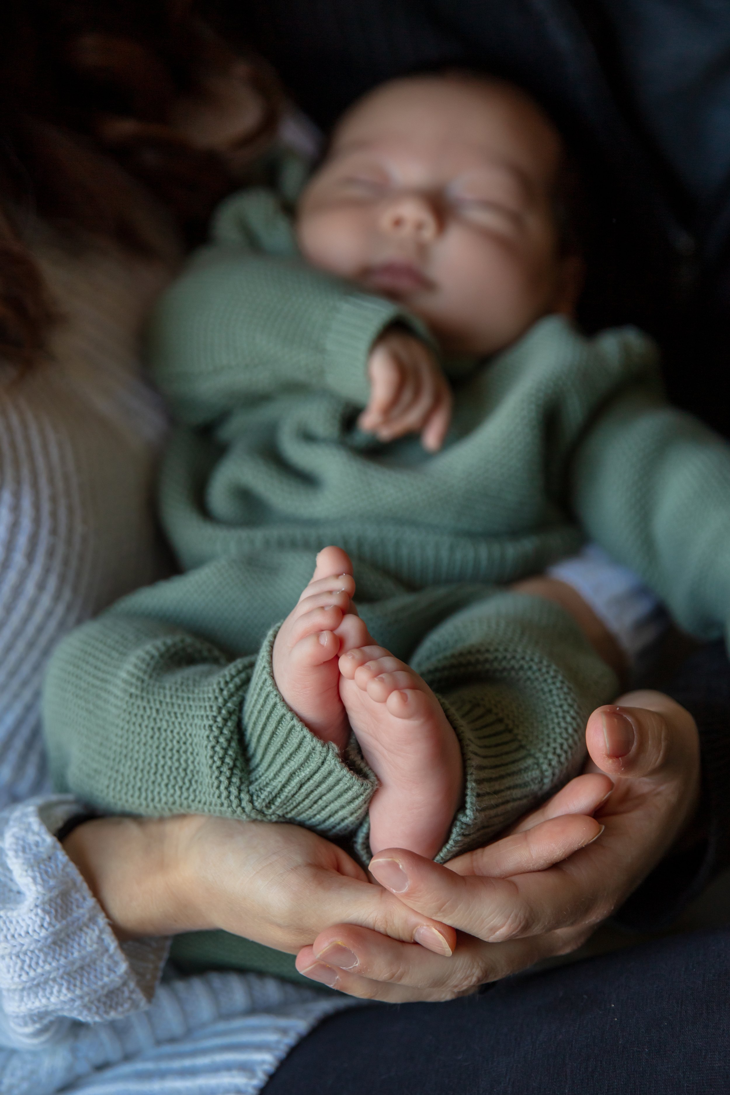 Newborn session, close up of mother and fathers hands together holding their baby's feet.