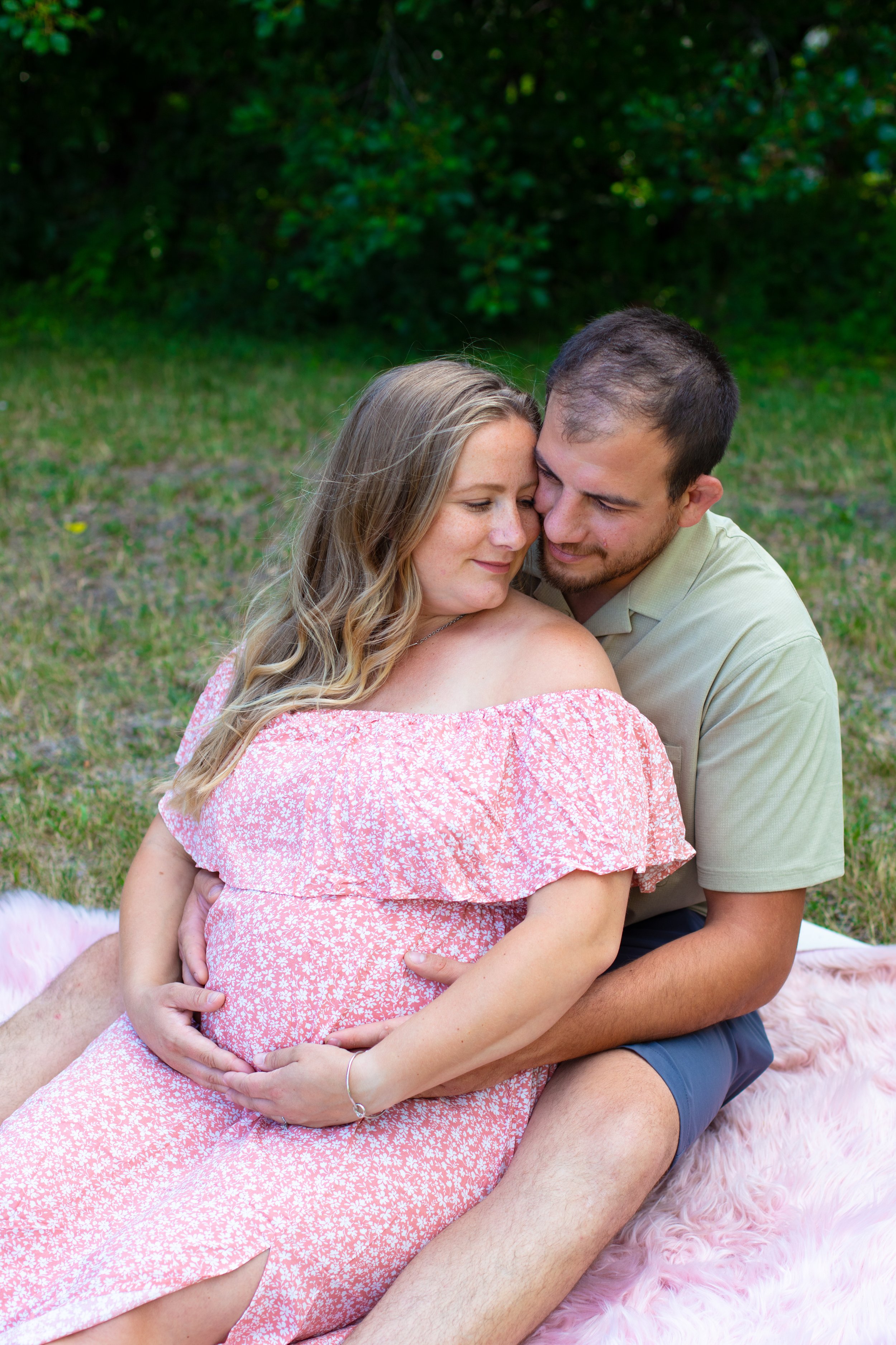 Maternity session - father and mother embracing each other while sitting on a blanket in the park