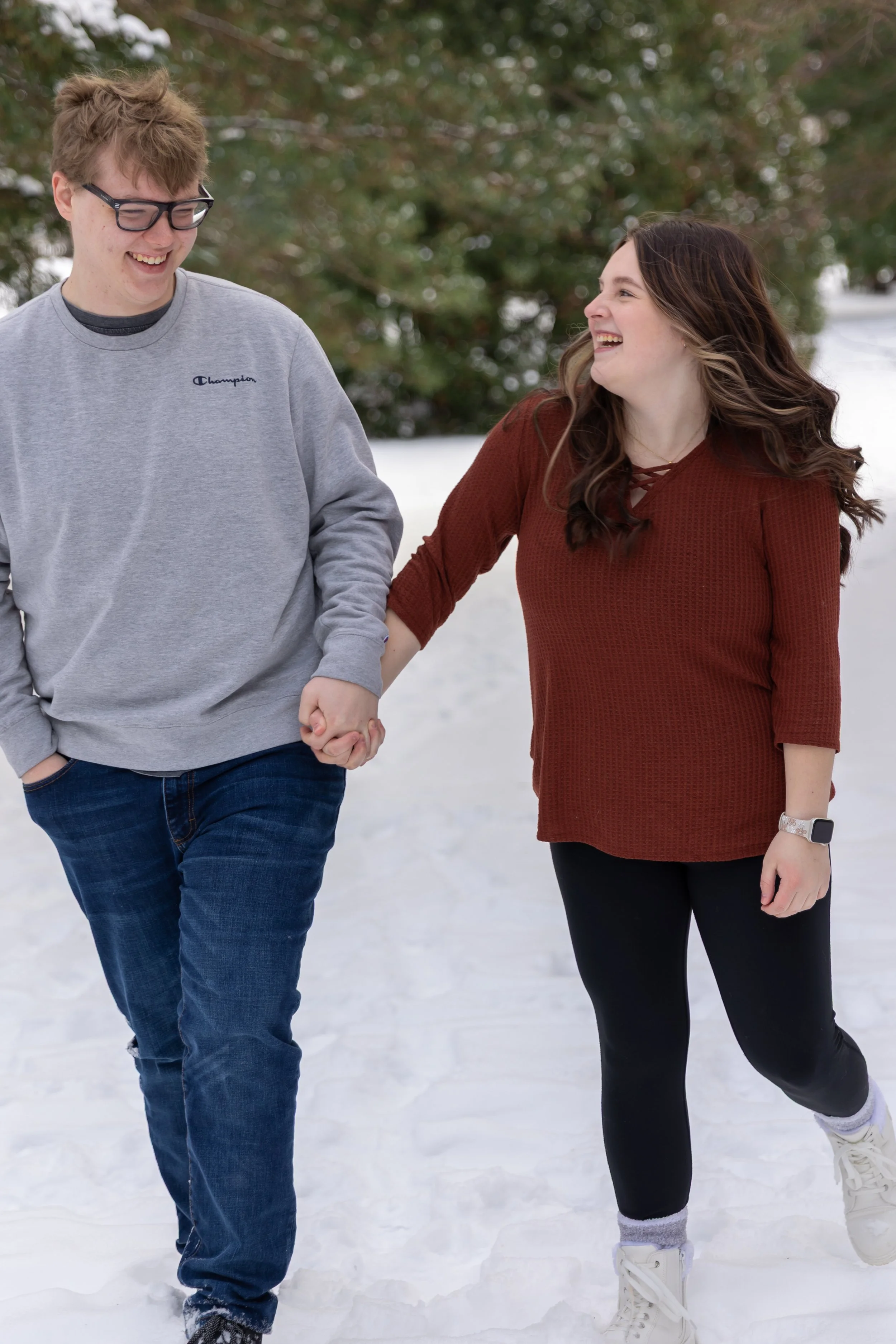 Minneapolis couples photography - A couple hold hands and walk towards the camera while laughing at each other in a winter scene at Arneson Acres Park in Edina, MN.