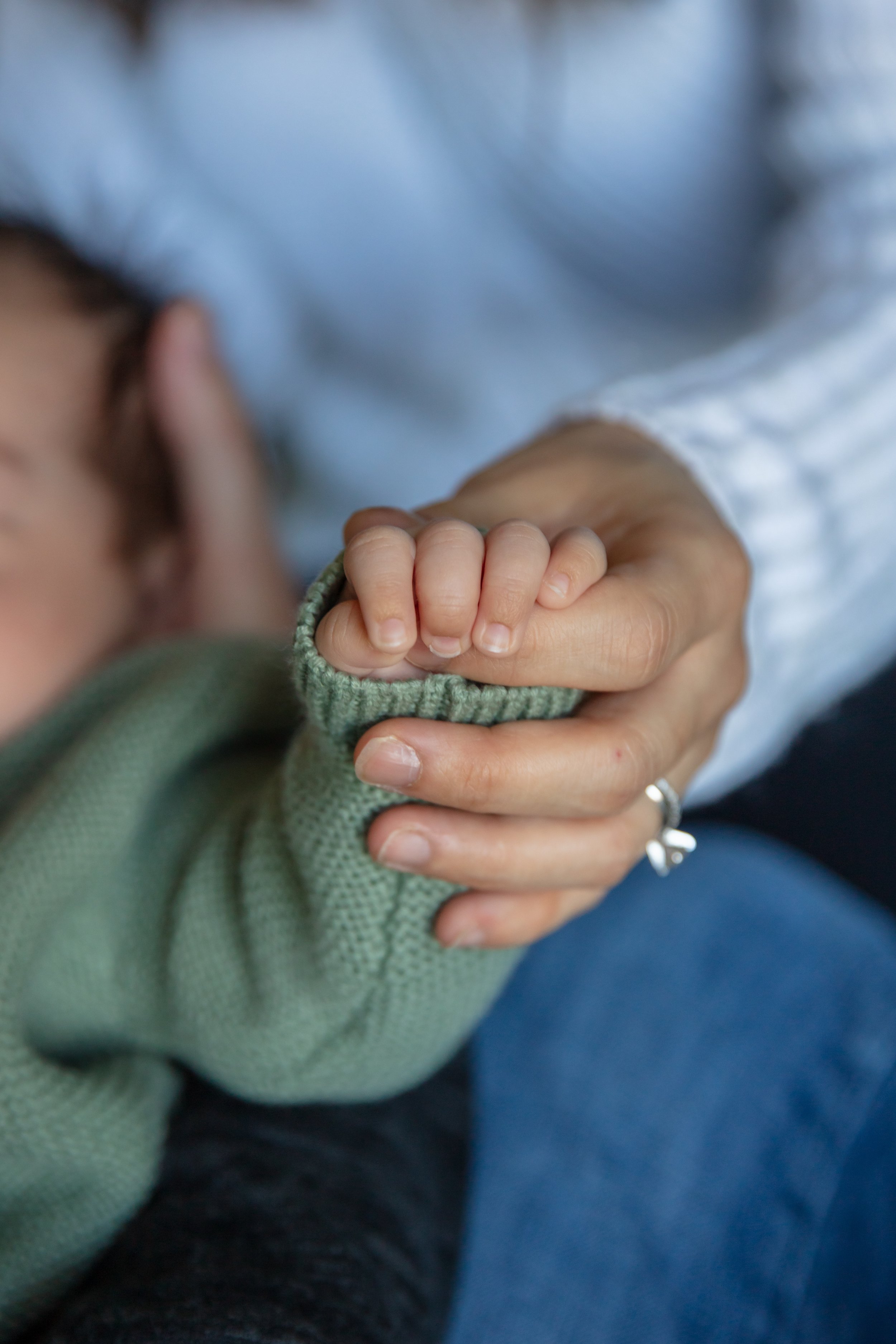 Newborn in-home session, close up of mom holding baby's hand with their fingers intertwined.