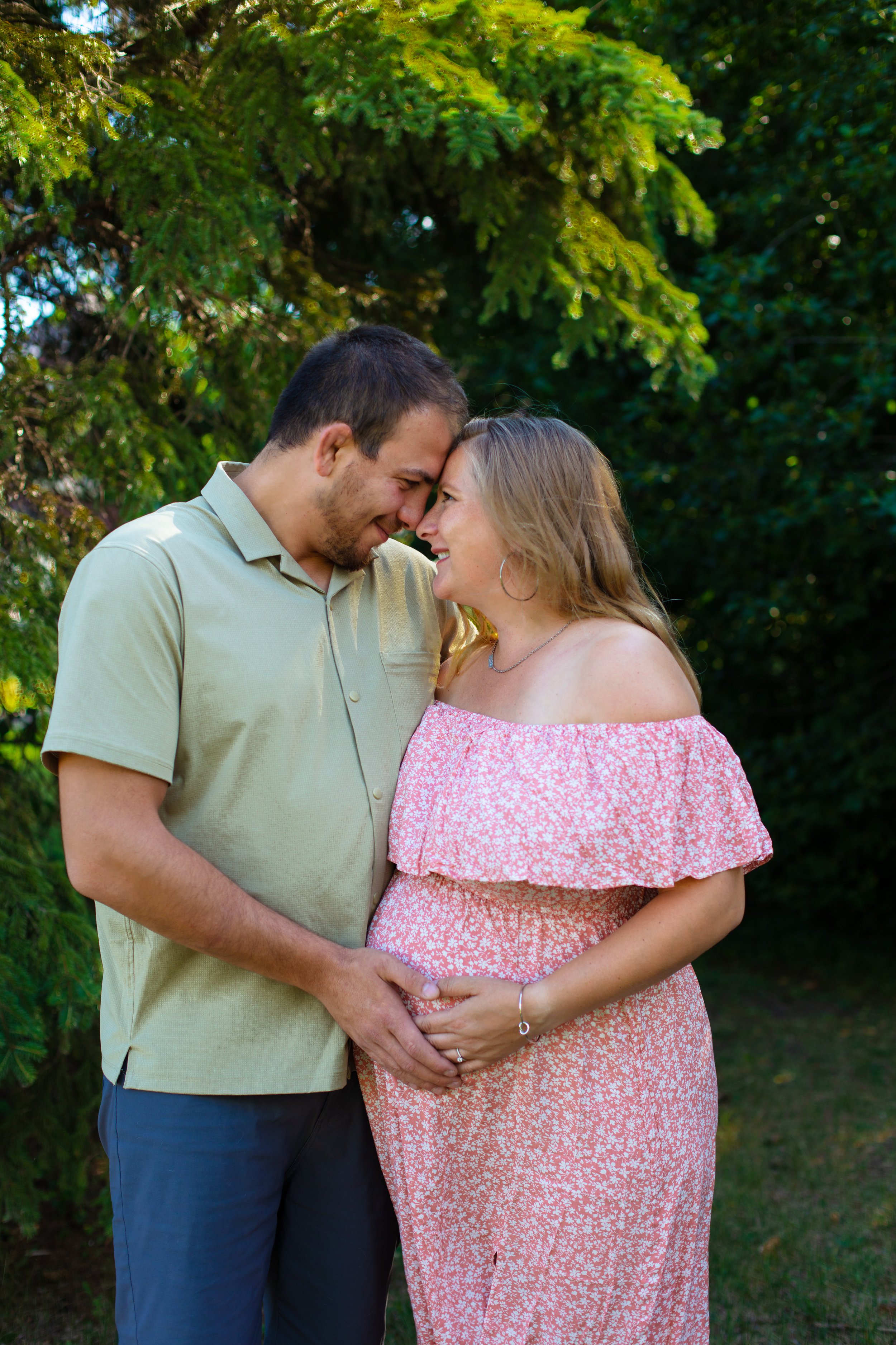 Maternity session - father and mother gaze lovingly at each other in the park while holding the baby bump