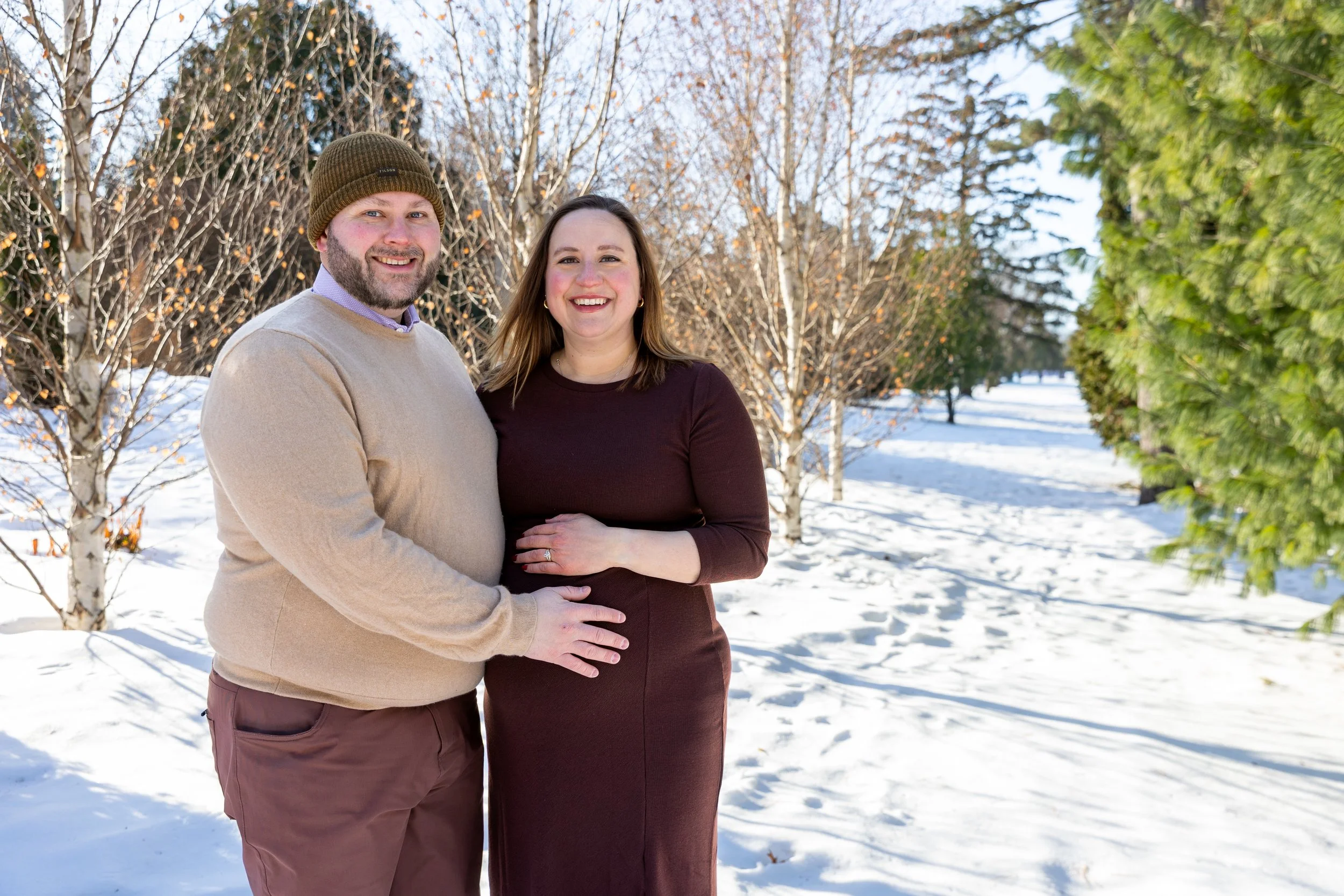 Maternity session, expecting mother and father-to-be embrace each other smiling at the camera at Arneson Acres Park in Edina, MN in the winter.