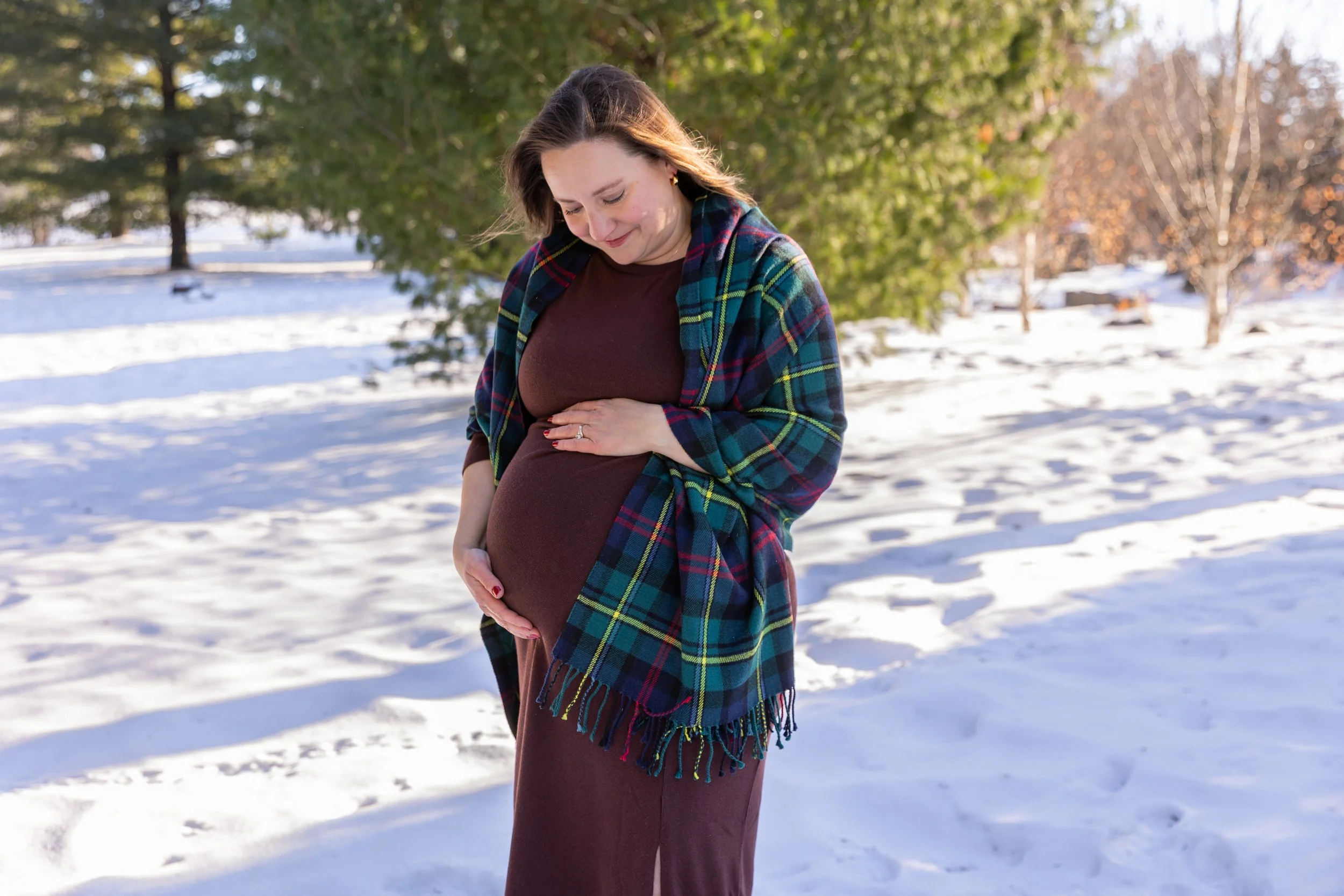 Minneapolis Maternity session, expecting mother cradling her baby bump smiling down at the bump while wearing a blanket at Arneson Acres Park in Edina, MN in the winter.