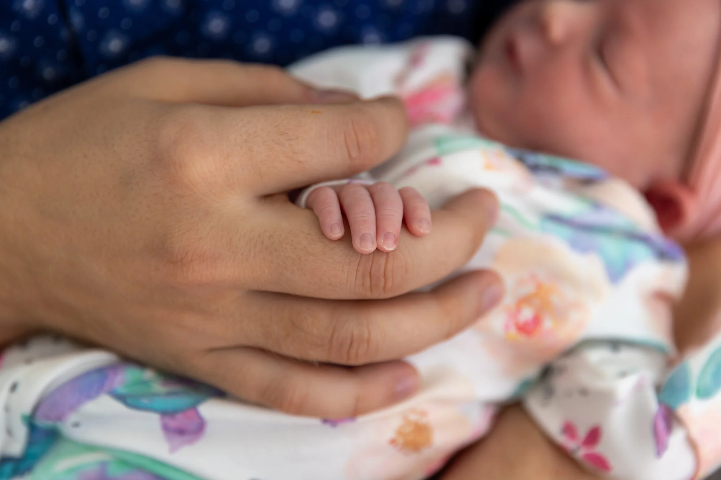 Minneapolis in-home newborn photography session - Up close image of newborn being held in the dads arms with the focus on the newborns fingers resting in the dads hand.
