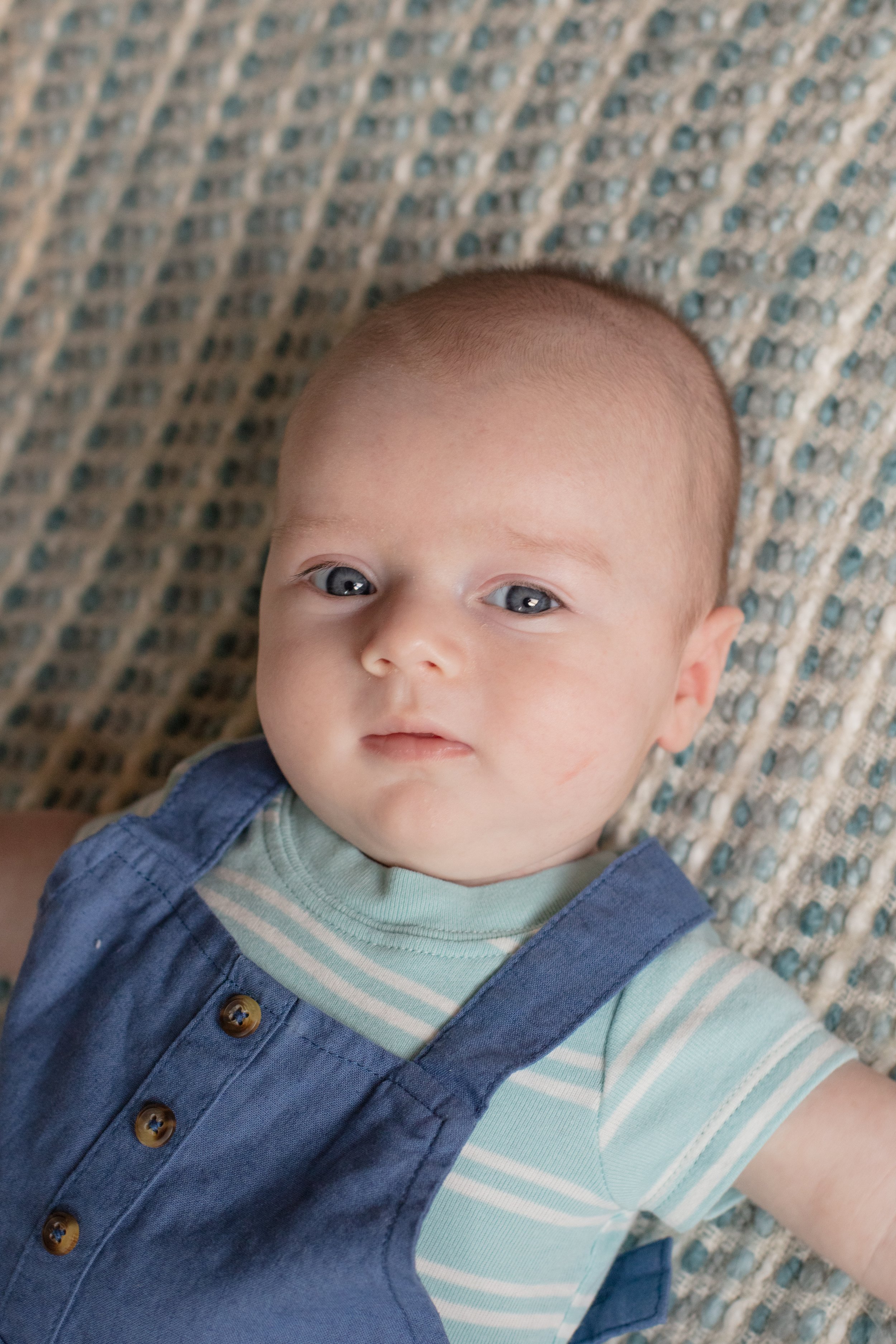Close up of baby laying down on his back while looking up at the camera.