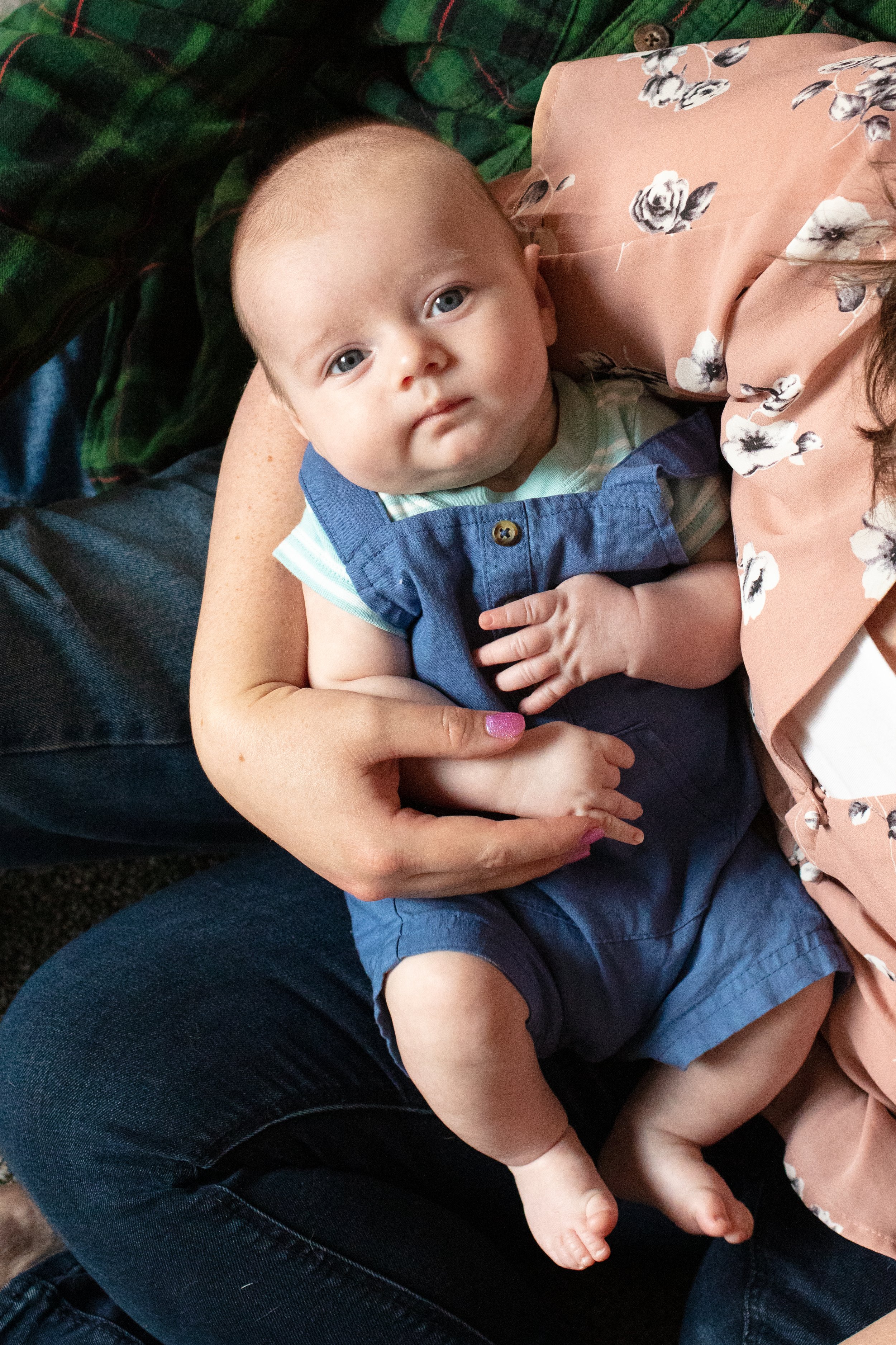 Close up image of baby being held in his mom's arms while looking up at the camera.