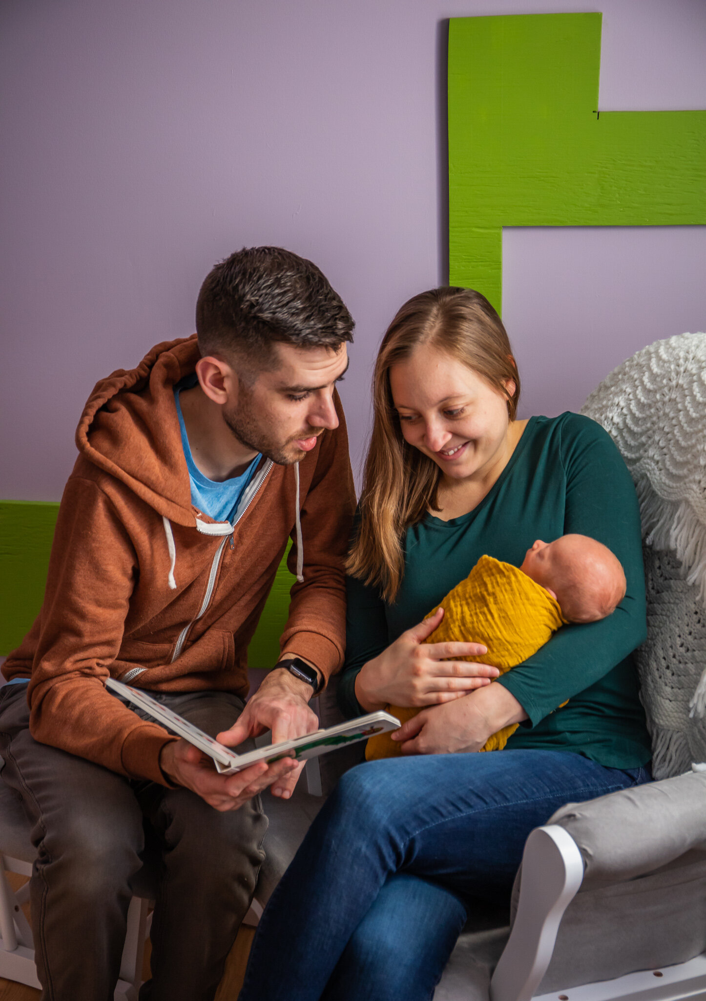 Newborn session, father and mother sitting reading a book to baby in home nursery
