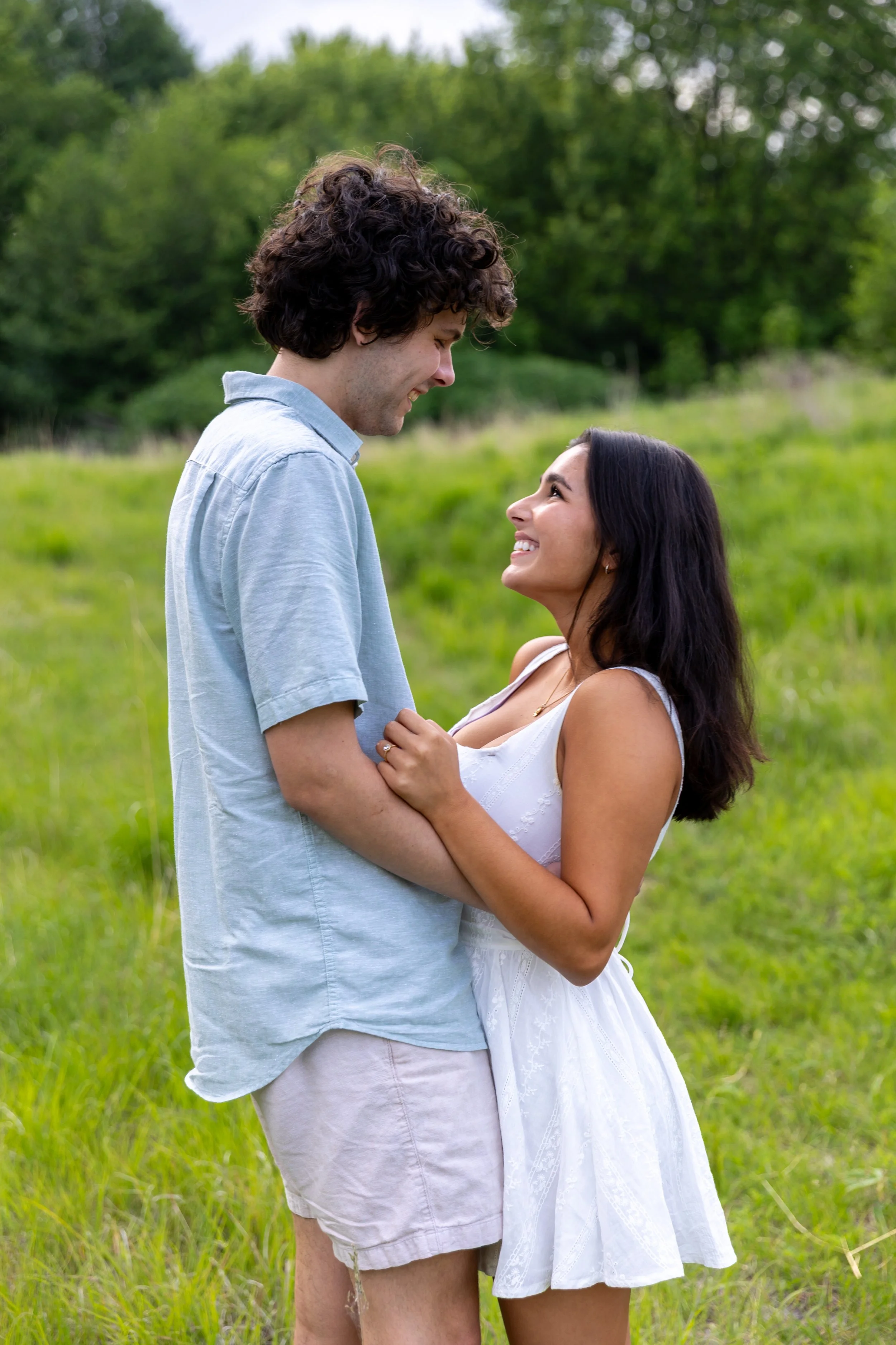 Minneapolis couples photography - A couple faces each other embraced in each others arms while smiling together standing in a grassy field smiling while at Minnehaha Falls Park in Minneapolis, MN. 