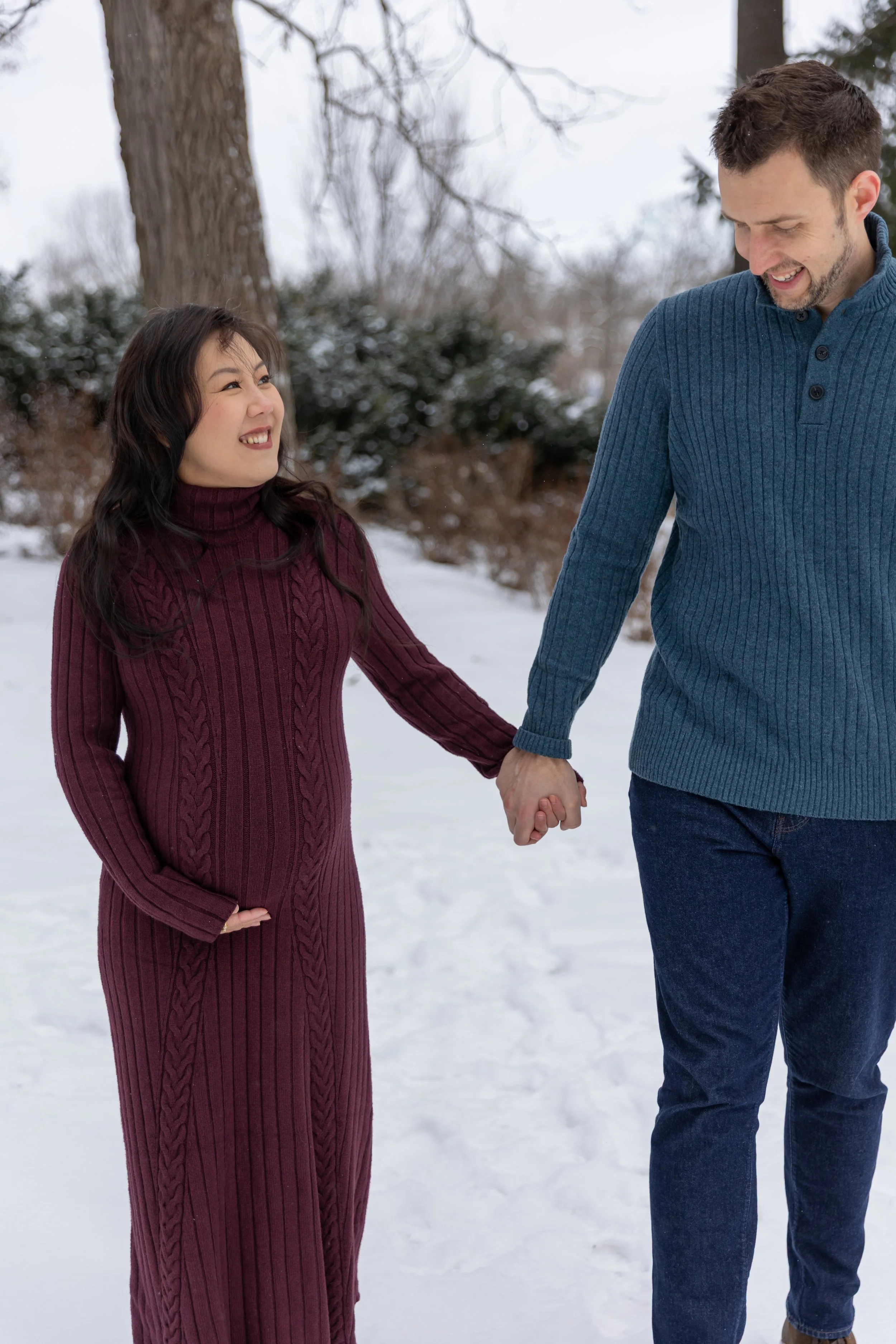 Minneapolis Maternity photography session - A soon to be mother and father walk towards the camera holding hands while smiling at each other at Minnetonka Mills Park in Hopkins, MN in the winter.