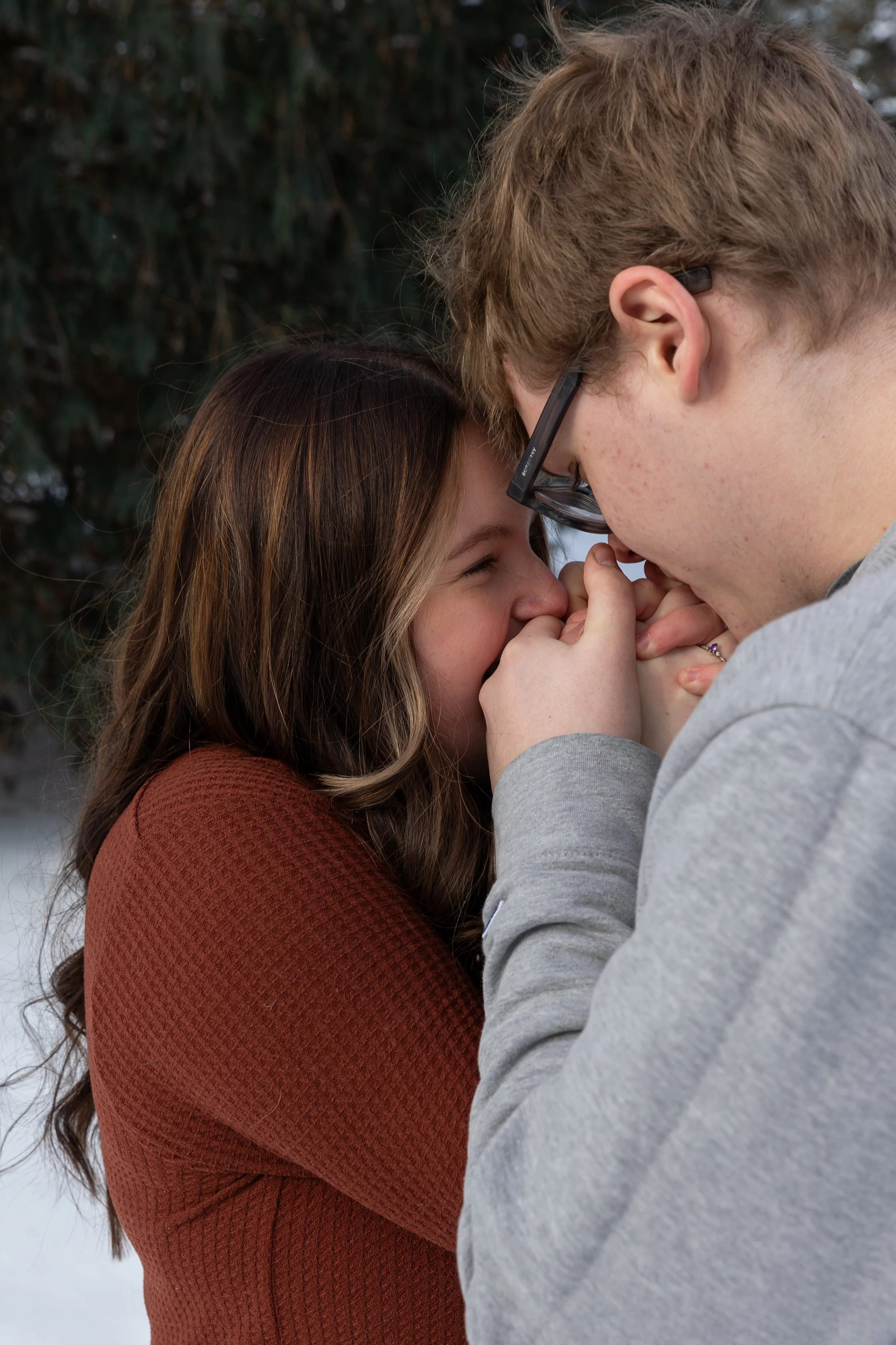 Minneapolis couples photography - A couple hold each others hands and are blowing on them to warm them up close to their faces while smiling at each other in a winter scene at Arneson Acres Park in Edina, MN.