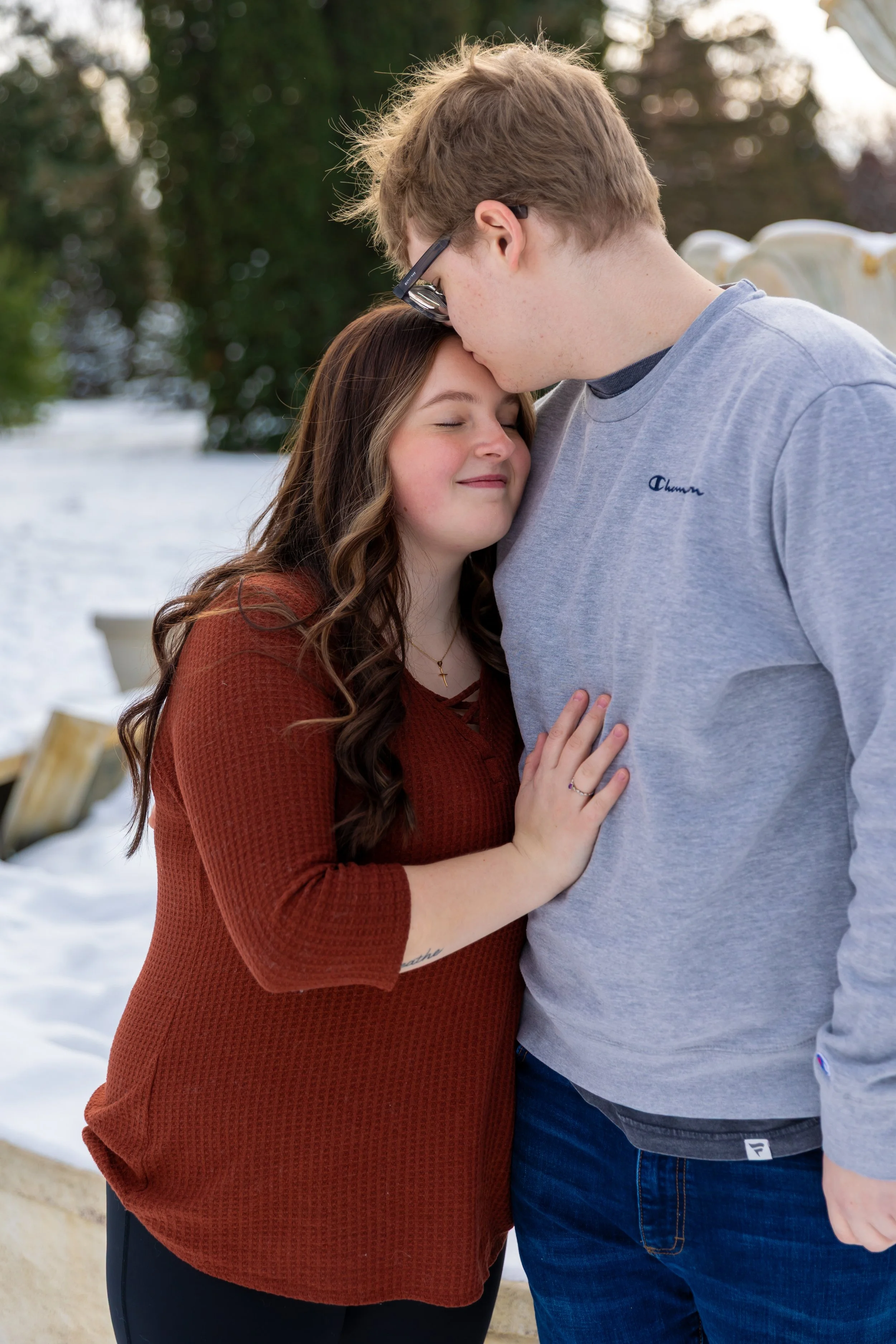 Minneapolis couples photography - A couple embrace each other with the man kissing the woman's forehead in a winter scene at Arneson Acres Park in Edina, MN.