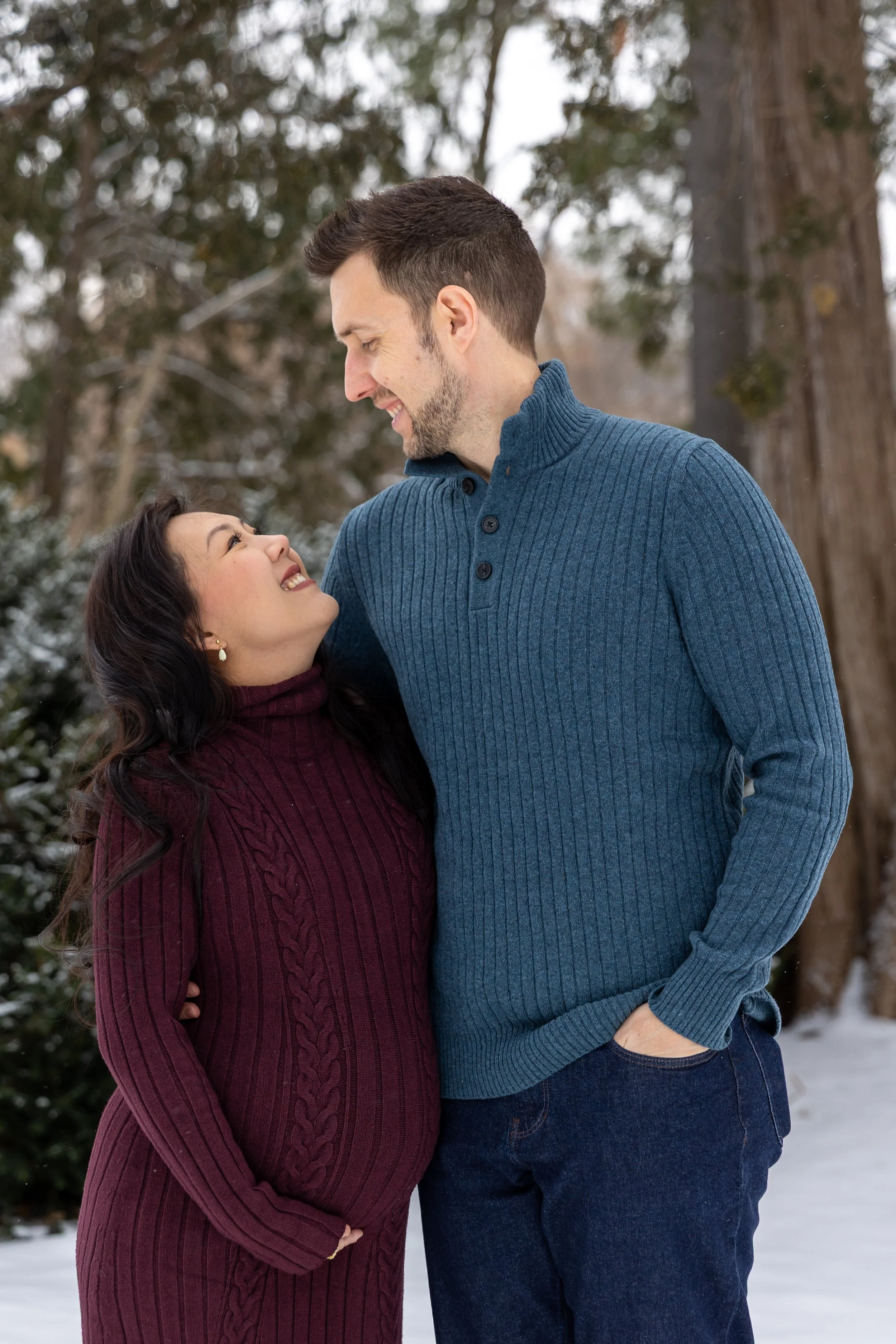 Minneapolis Maternity photography session - A soon to be mother and father stand embracing each other side by side while smiling at each other at Minnetonka Mills Park in Hopkins, MN in the winter.