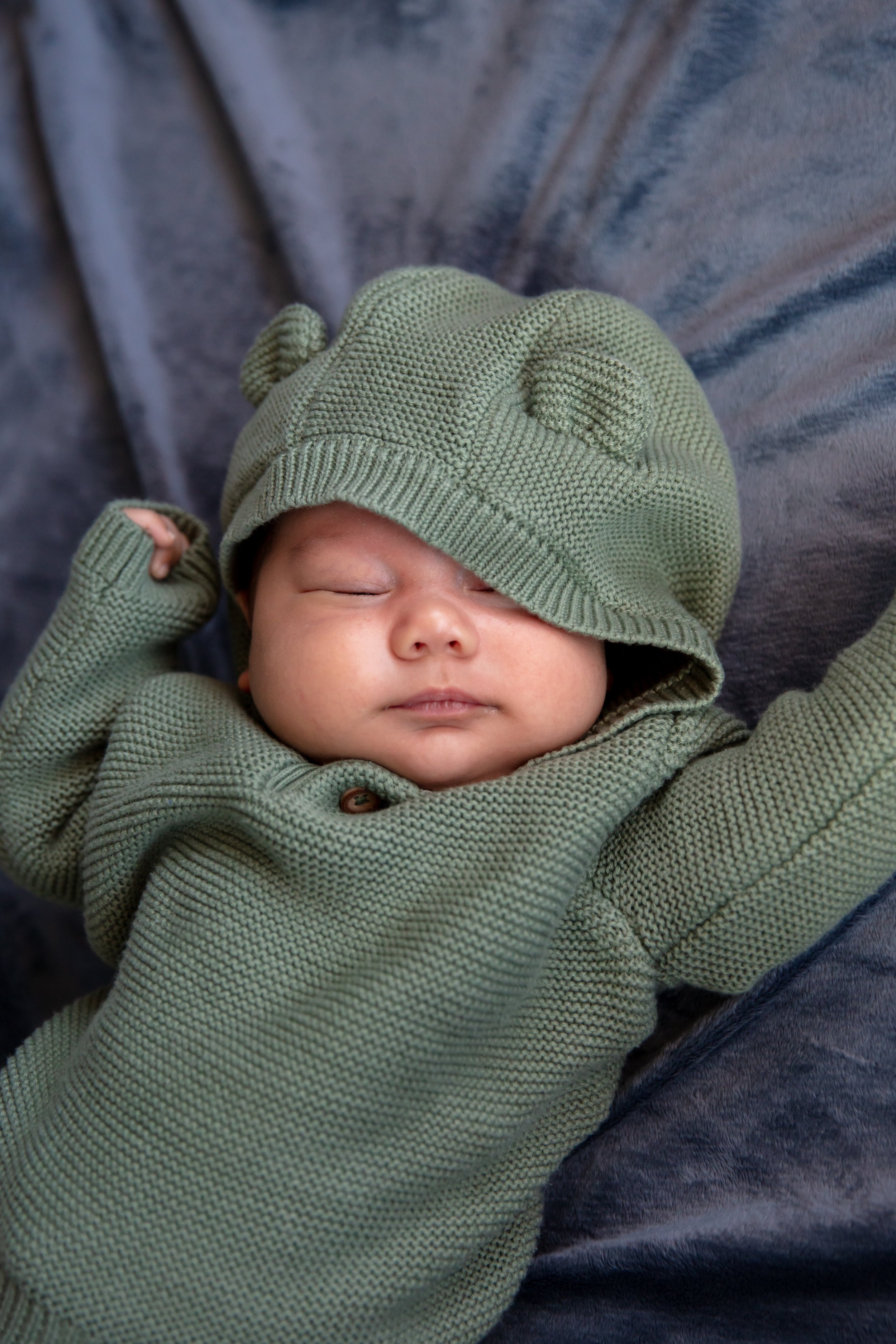 Close up of baby sleeping in a onesie with bear ears on the hood while laying on a blanket.
