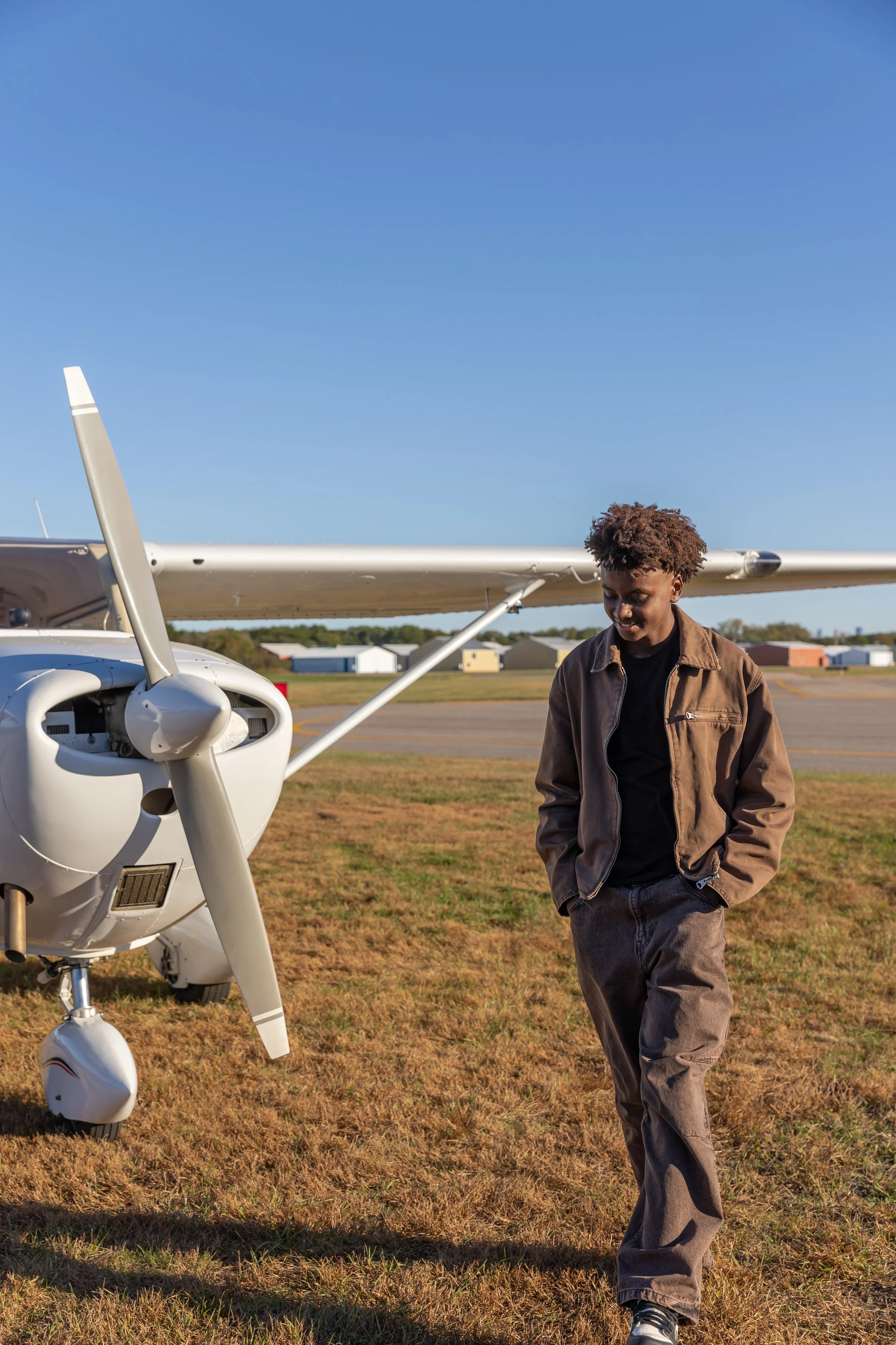 A Maple Grove high school senior walks with his hands in his pockets in front of a Cessna airplane in the Crystal airport for their senior photos.