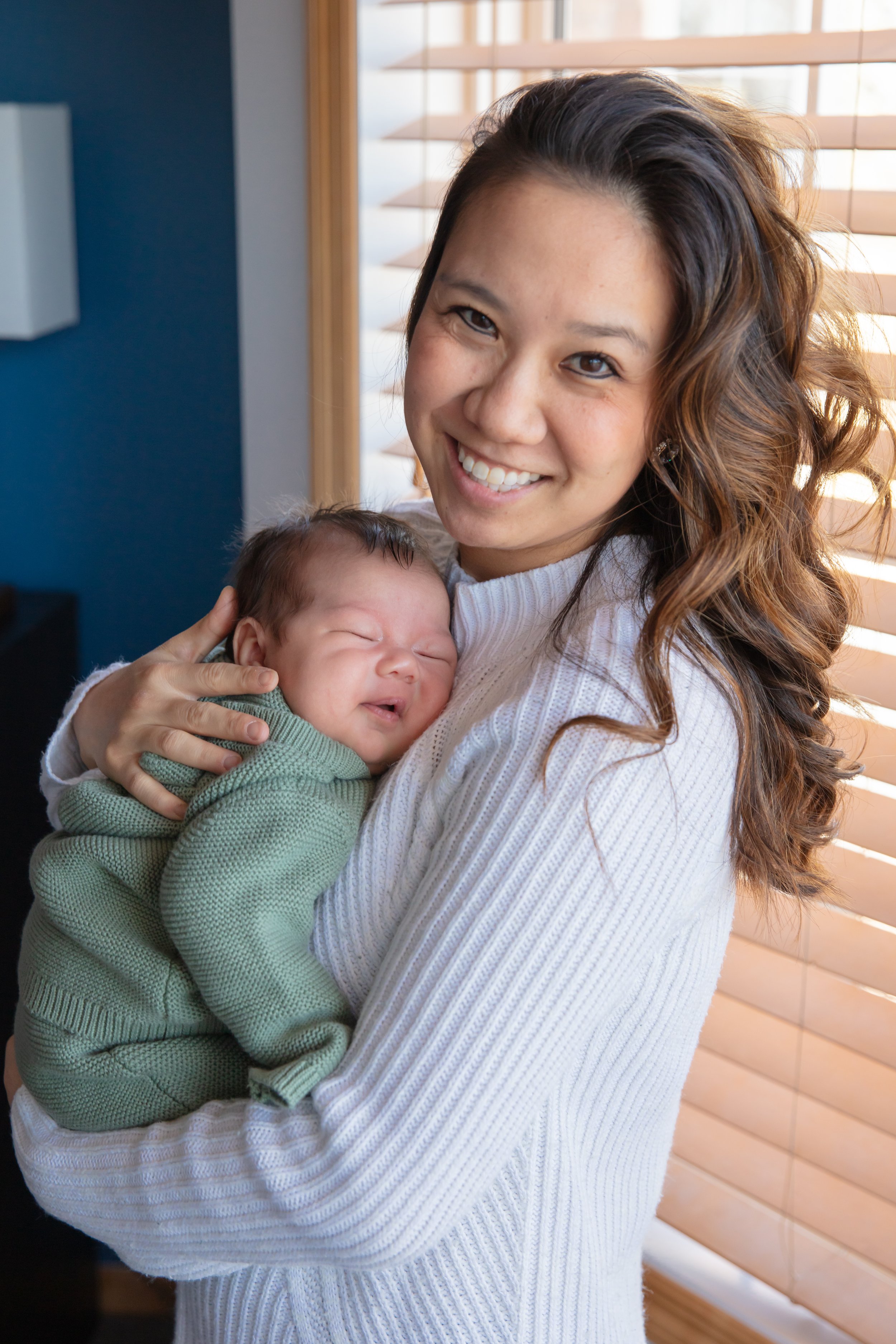Mom holds her baby in her arms as she smiles at the camera.