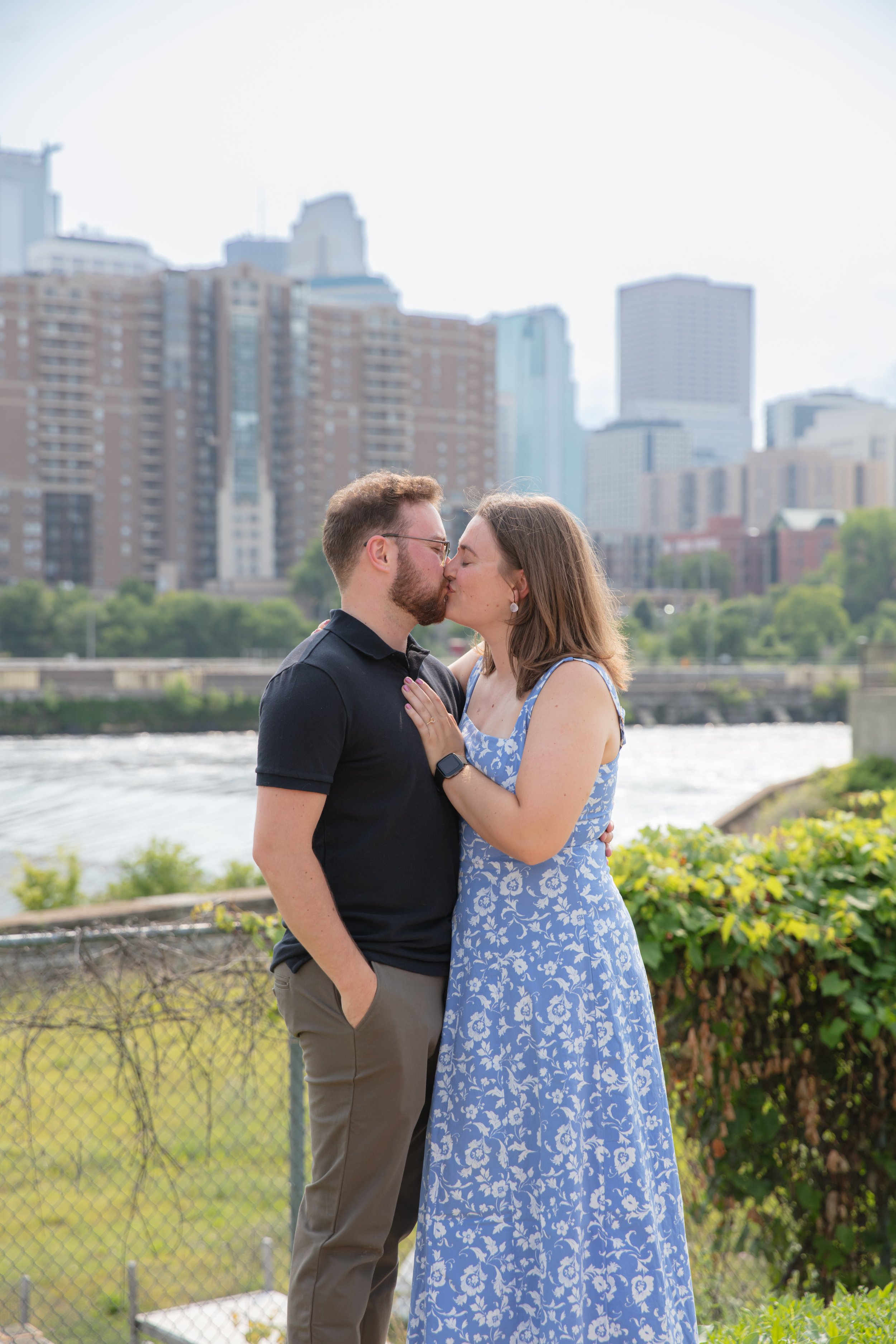 A couple, a man and woman, embraces each other kissing after he proposed to her in front of the falls and skyline at Water Power Park on St. Anthony Main.
